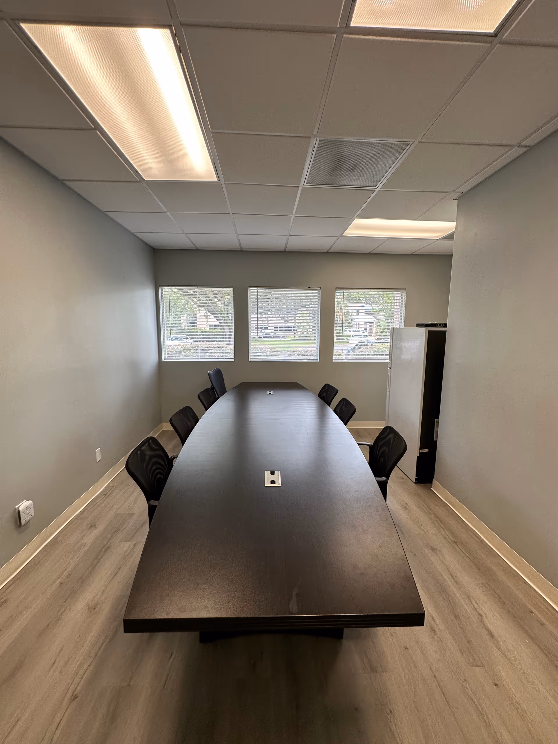 Long dark conference table with chairs in a narrow windowed meeting room.