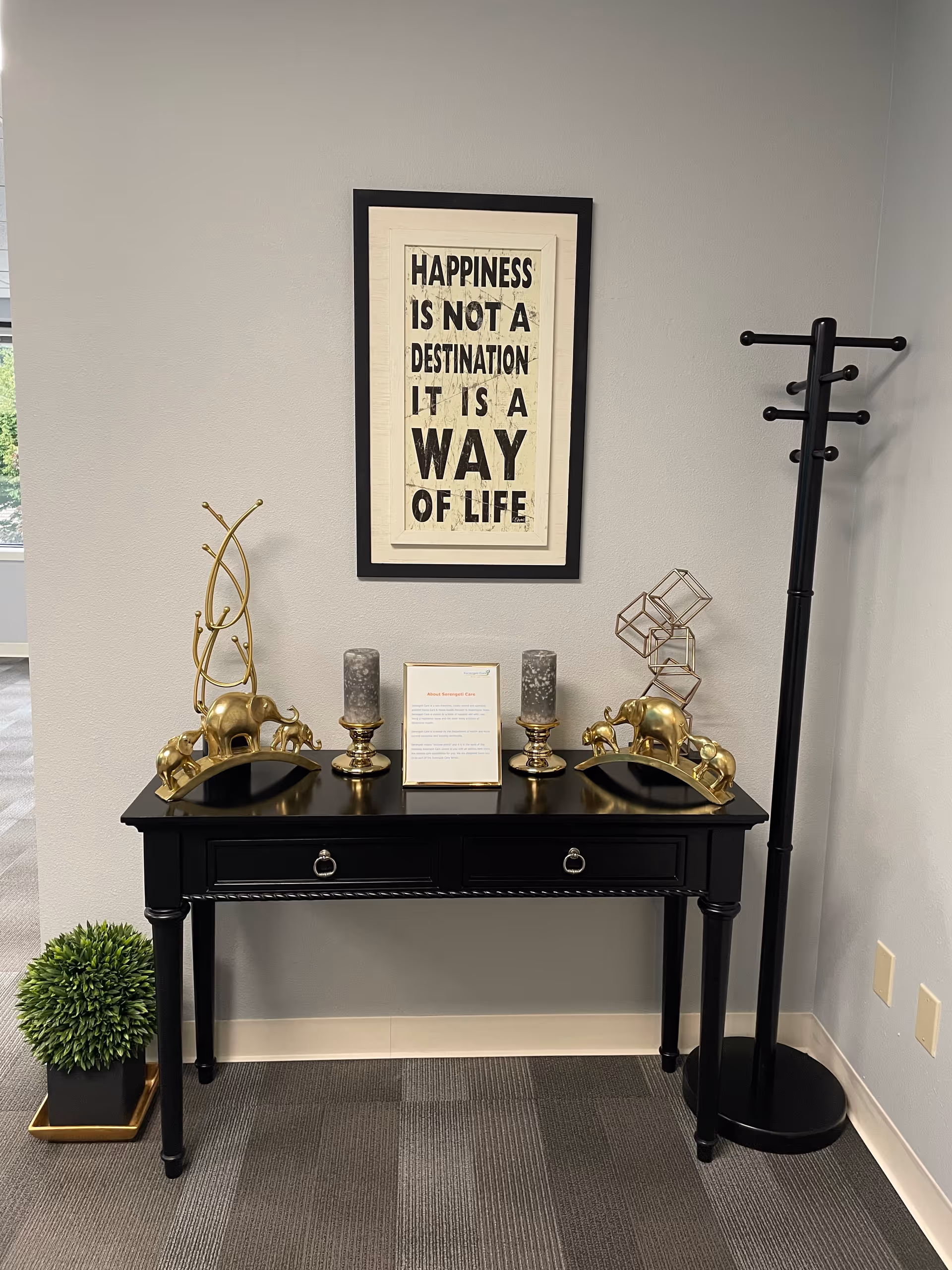 Black console table with framed motivational art and golden decor pieces against a gray wall.