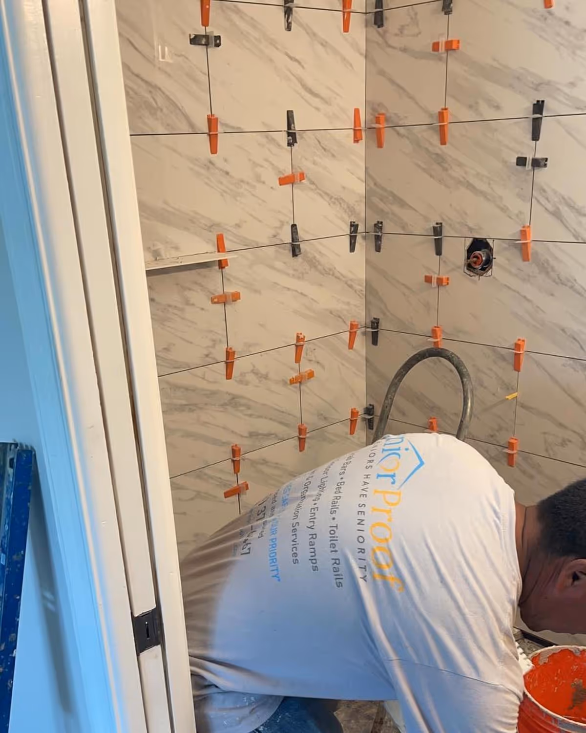 Construction worker tiling a bathroom wall with orange spacers