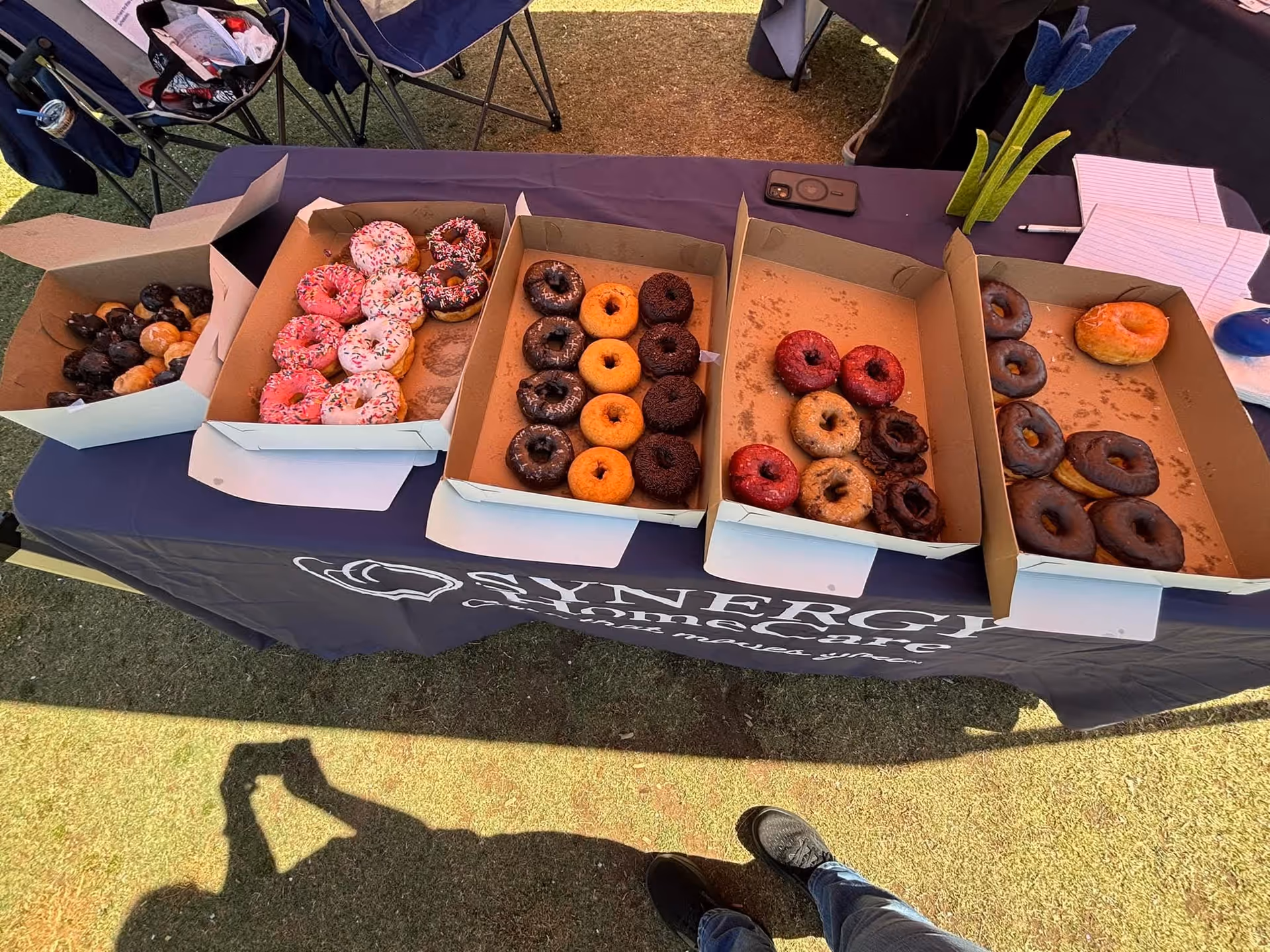 Outdoor tablecloth with Synergy HomeCare branding and boxes of assorted donuts.