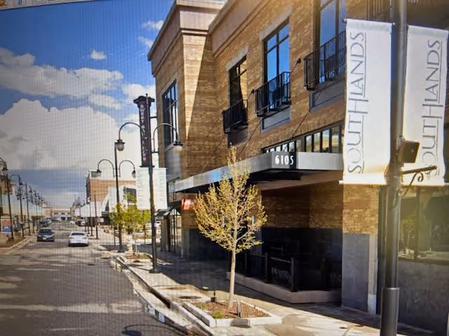 Street view of a modern building exterior with banners and trees along sidewalk.