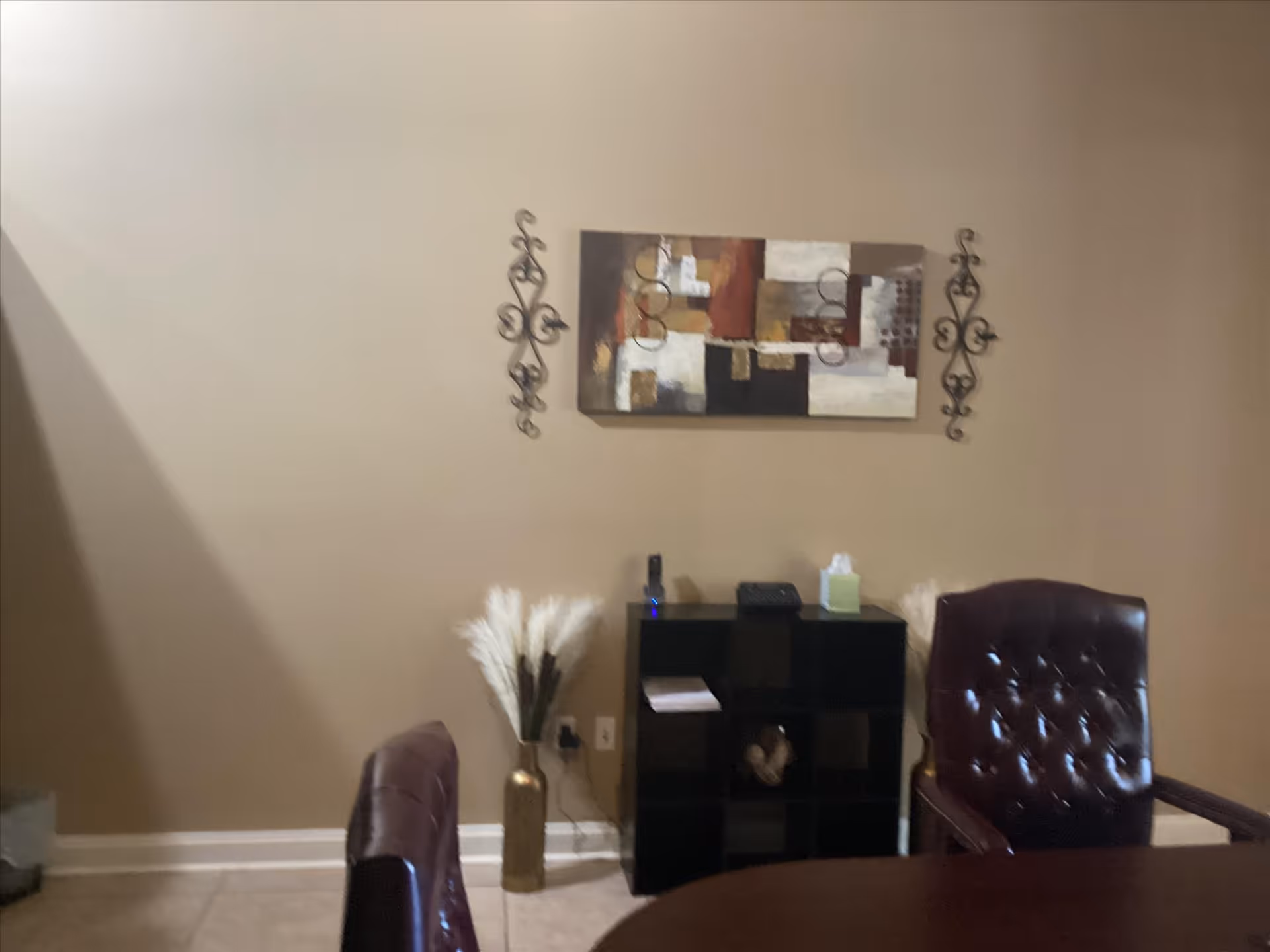 Beige walls, abstract wall art, black cubby shelf, vase, and round table with leather chairs.