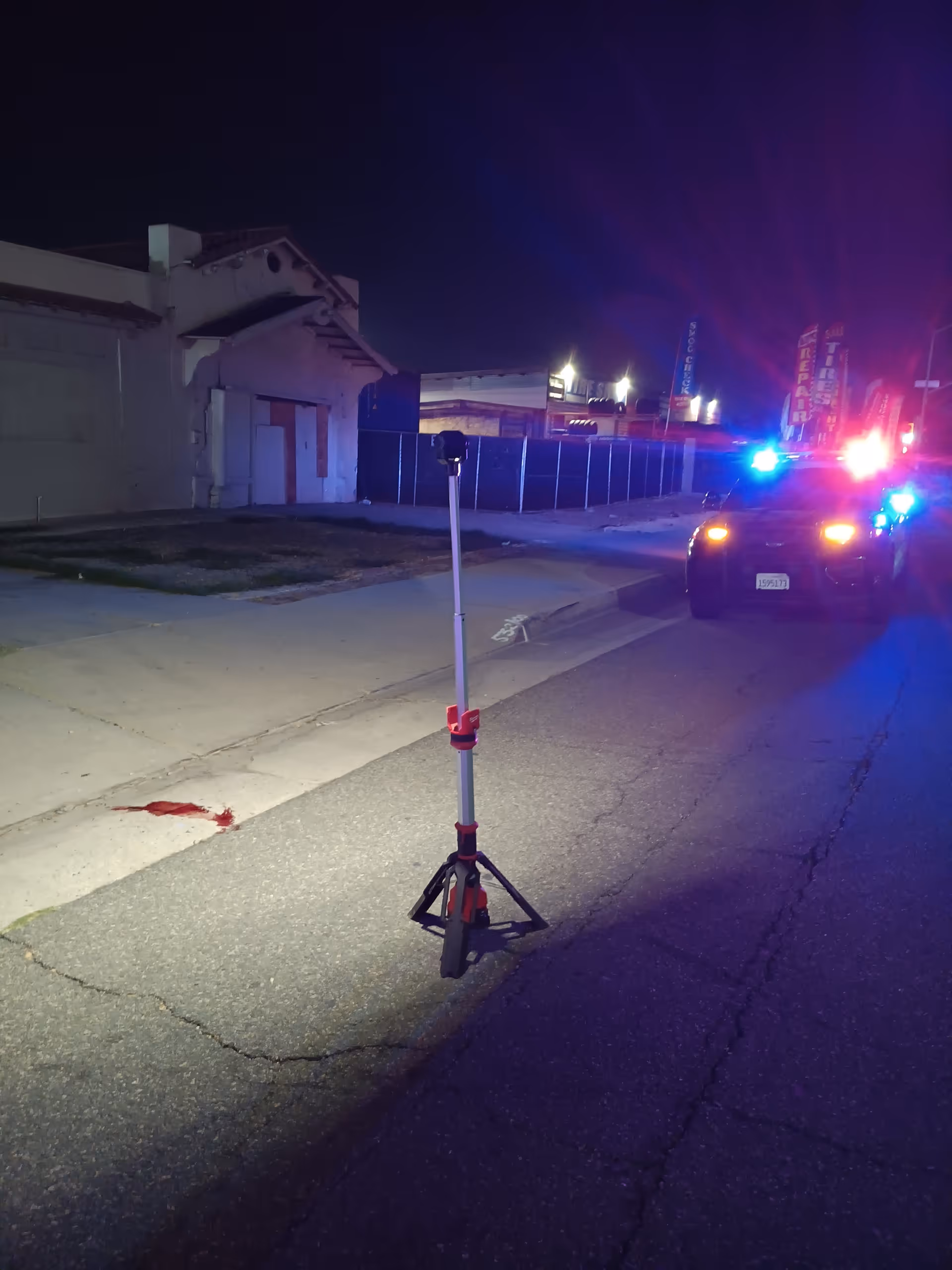 Nighttime street scene with police car flashing lights and a portable tripod in the road