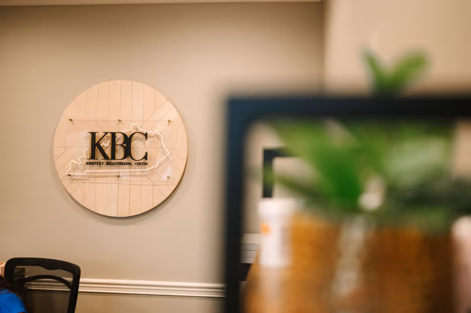 A circular wooden sign reading KBC Kentucky Breastfeeding Center on a light interior wall.