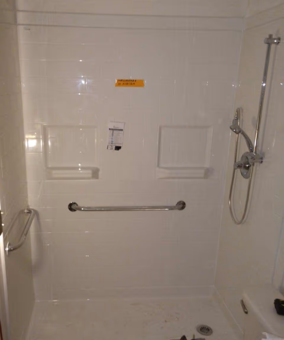 Walk-in bathroom shower with white tile walls, grab bars, and built-in shelves.