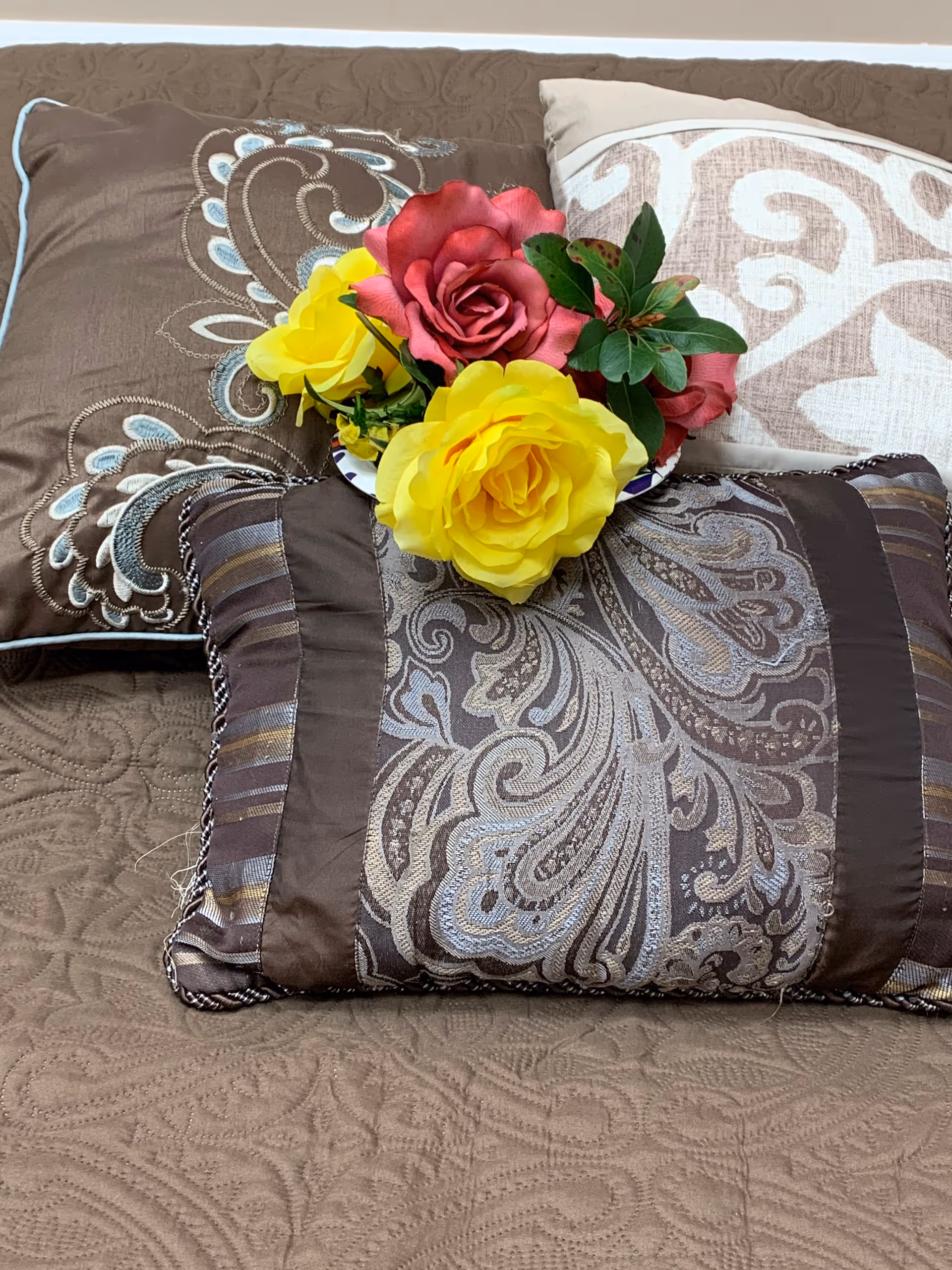 A brown patterned sofa features decorative pillows and a colorful bouquet of flowers.