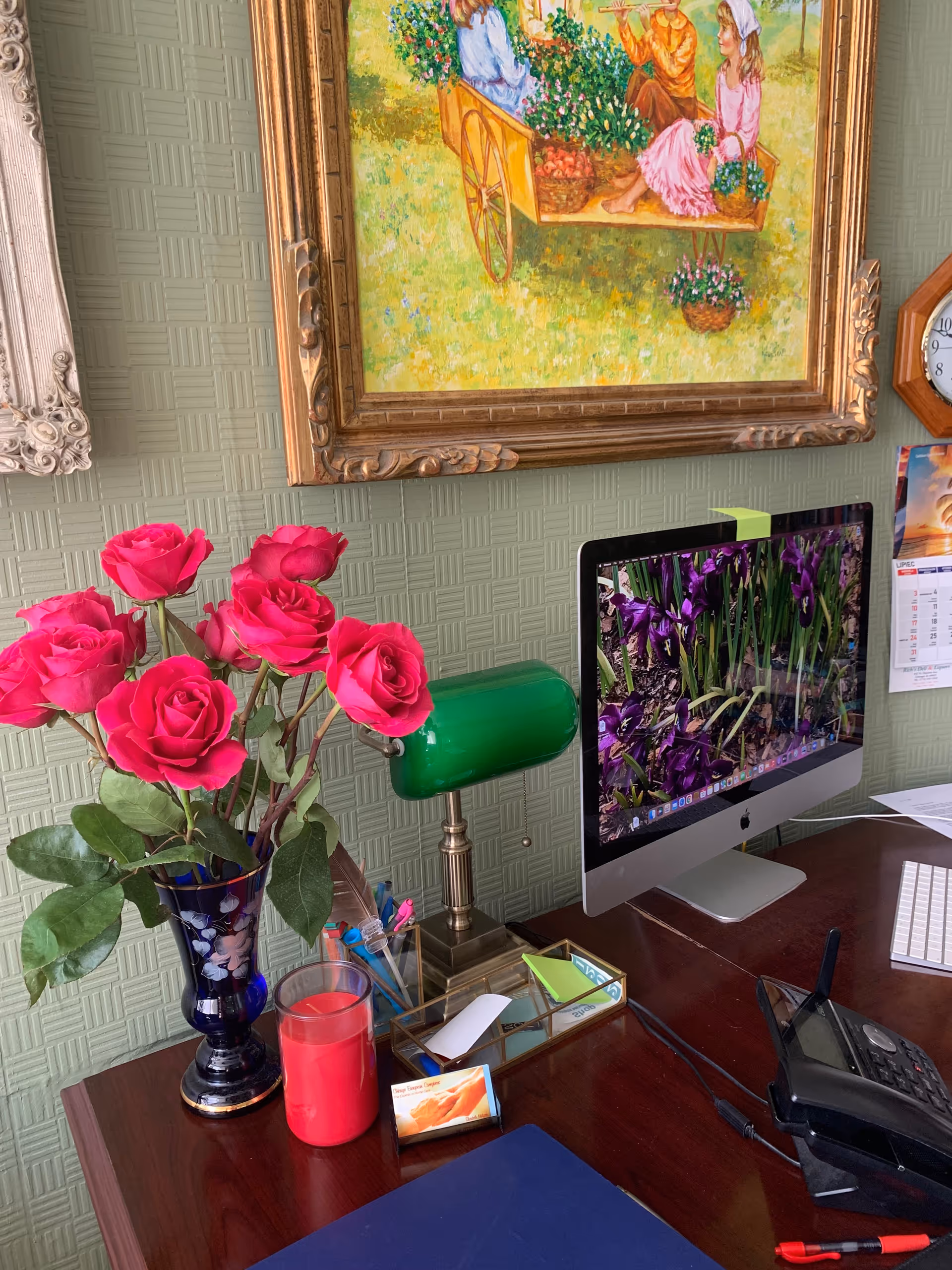 Desk with pink roses, a green lamp, and an iMac against a patterned green wall.