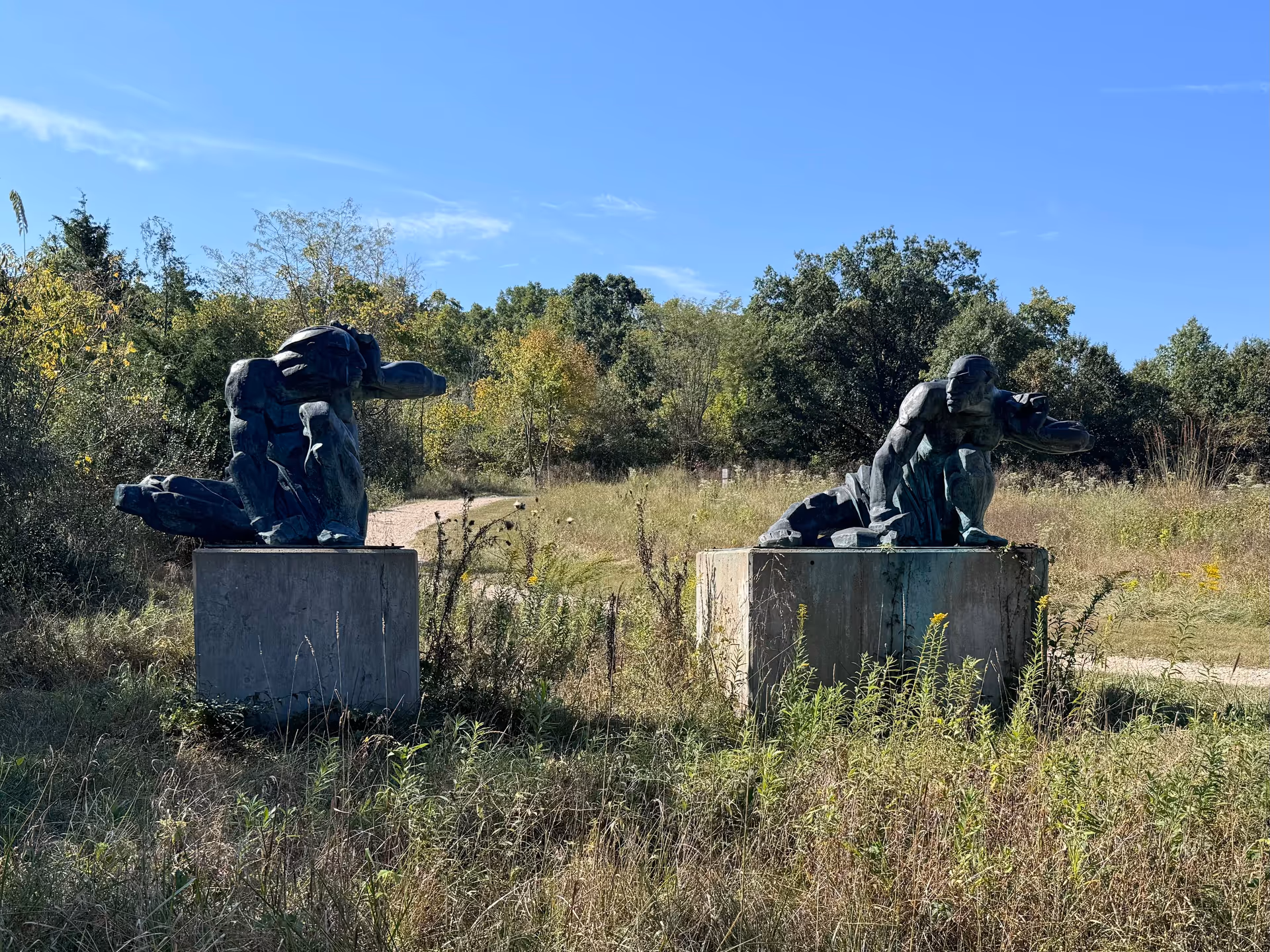 Two abstract statues on concrete pedestals in a grassy outdoor area.