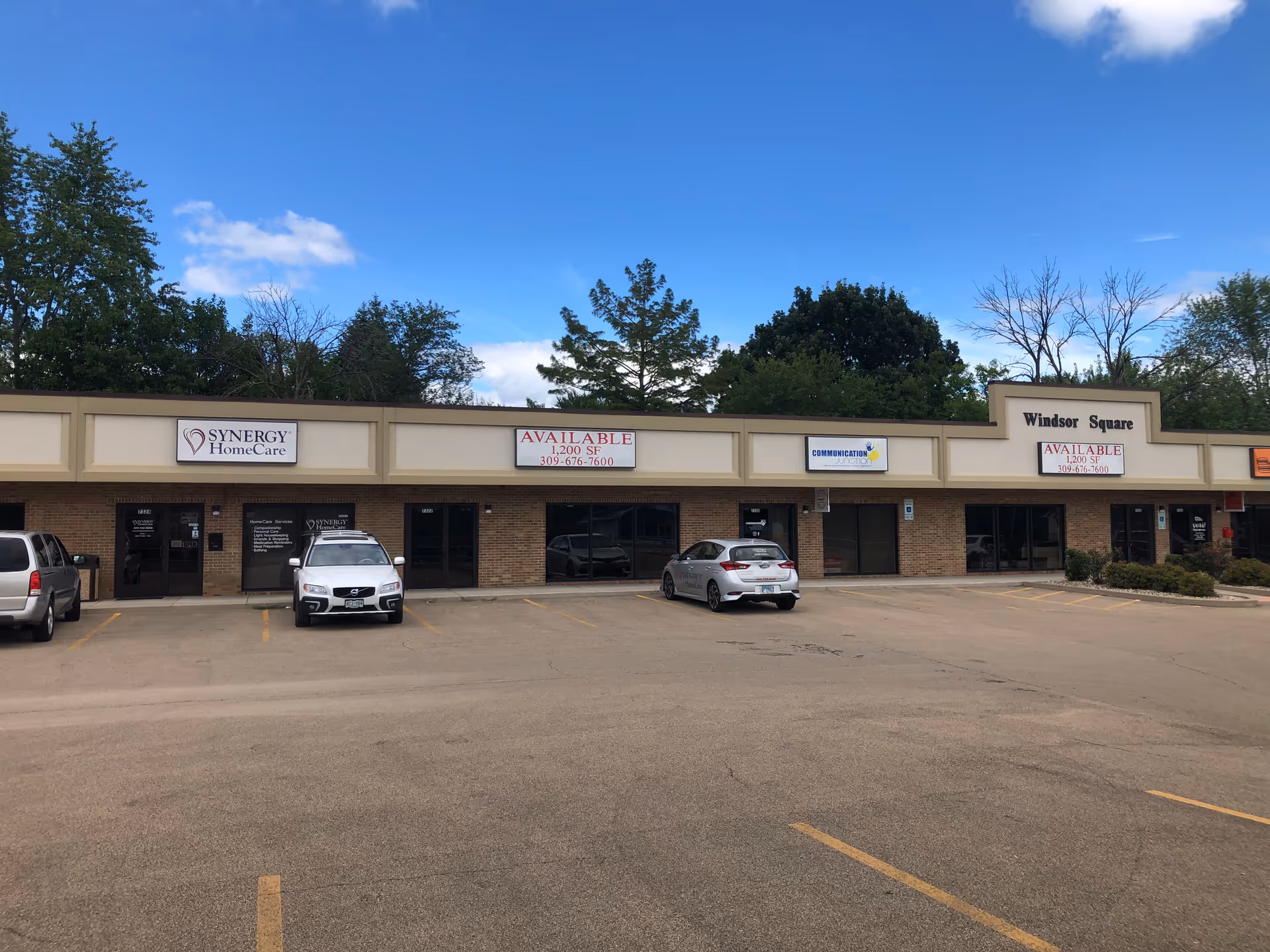 Strip mall storefronts with Synergy HomeCare sign, parked cars, and a blue sky.