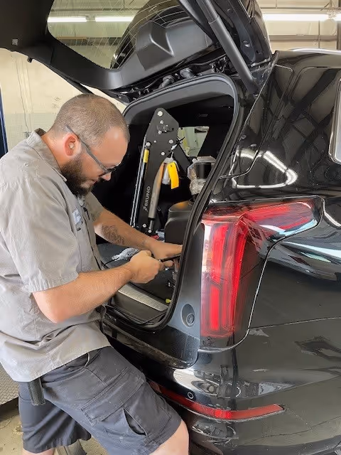 A technician works on a wheelchair lift inside a black SUV.
