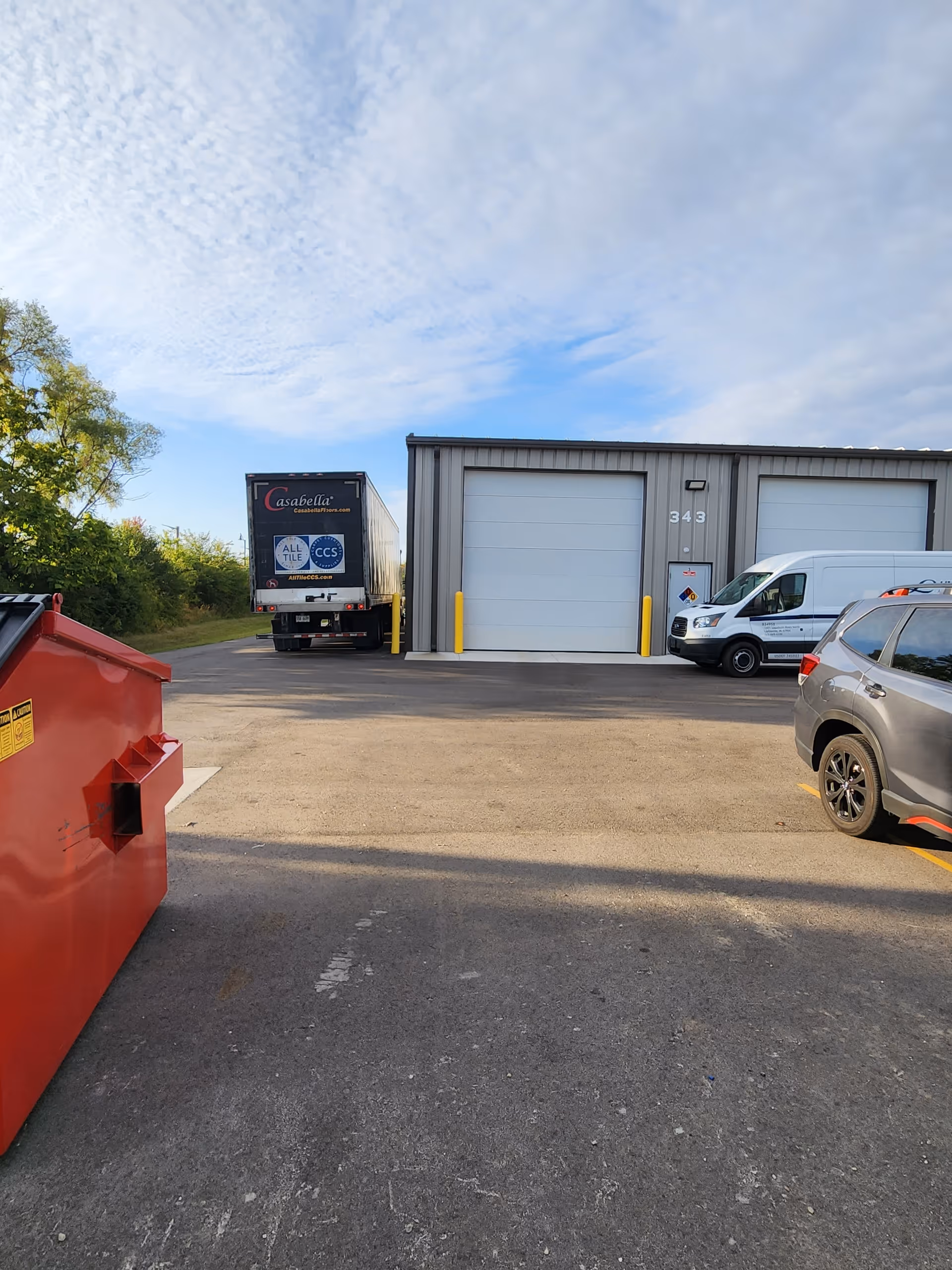 Exterior view of a LinCare facility with garage bays, vehicles, and a red dumpster.