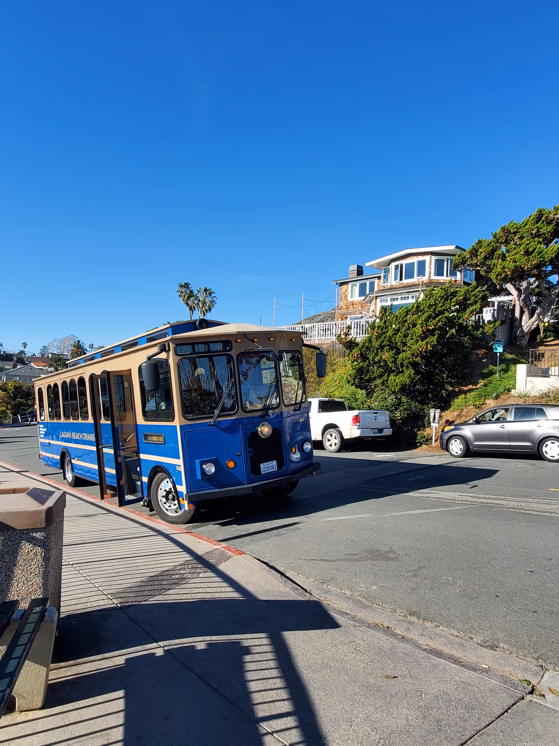 Blue vintage bus on a sunny street with hillside houses and blue sky.