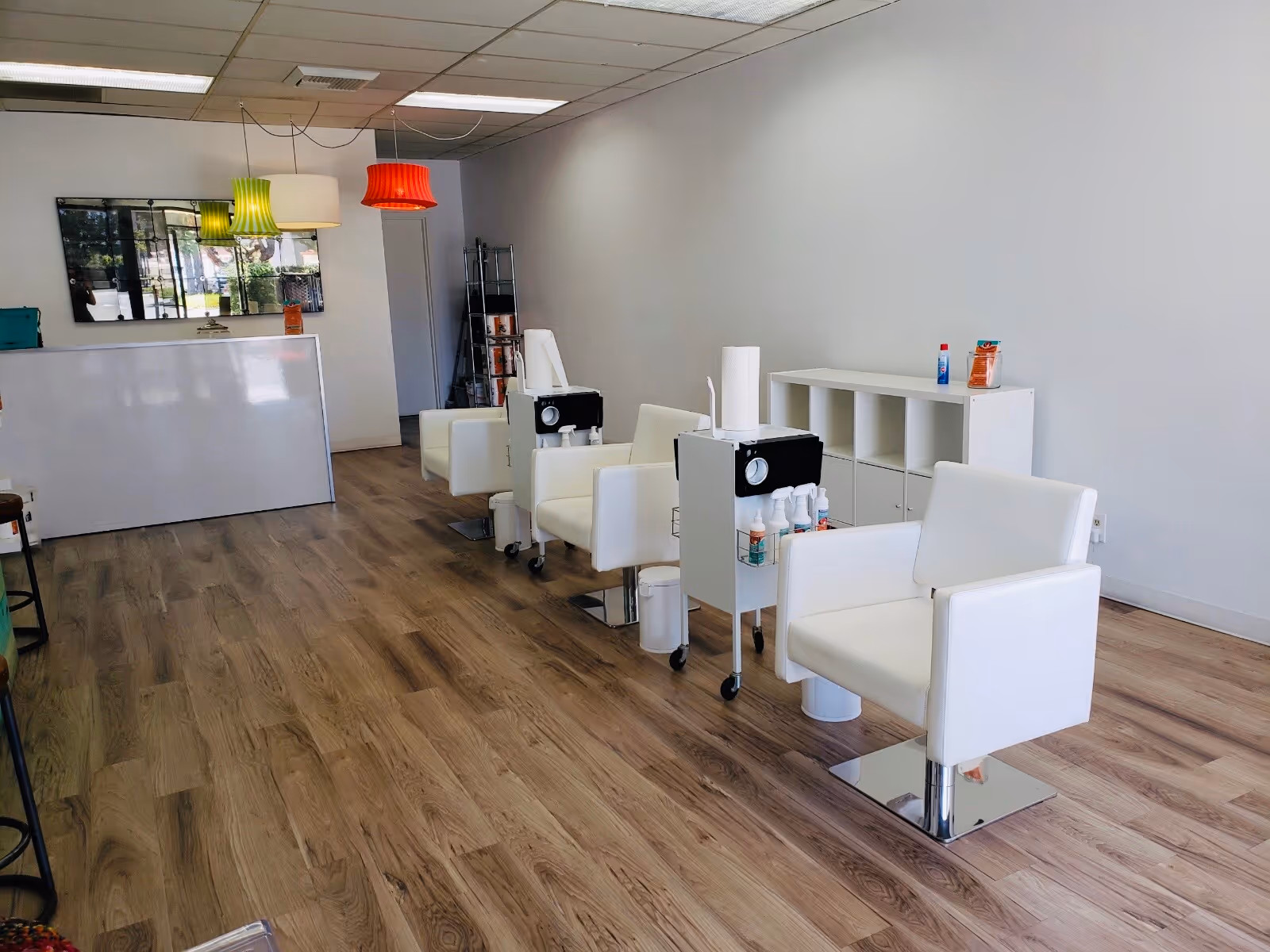 Bright, modern salon interior with white chairs, carts, and colorful hanging lamps.