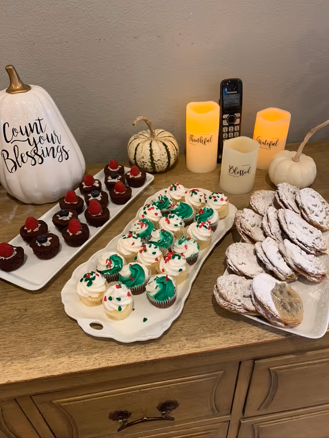 Assorted desserts on a wooden counter, flanked by pumpkins, candles, and fall decor.