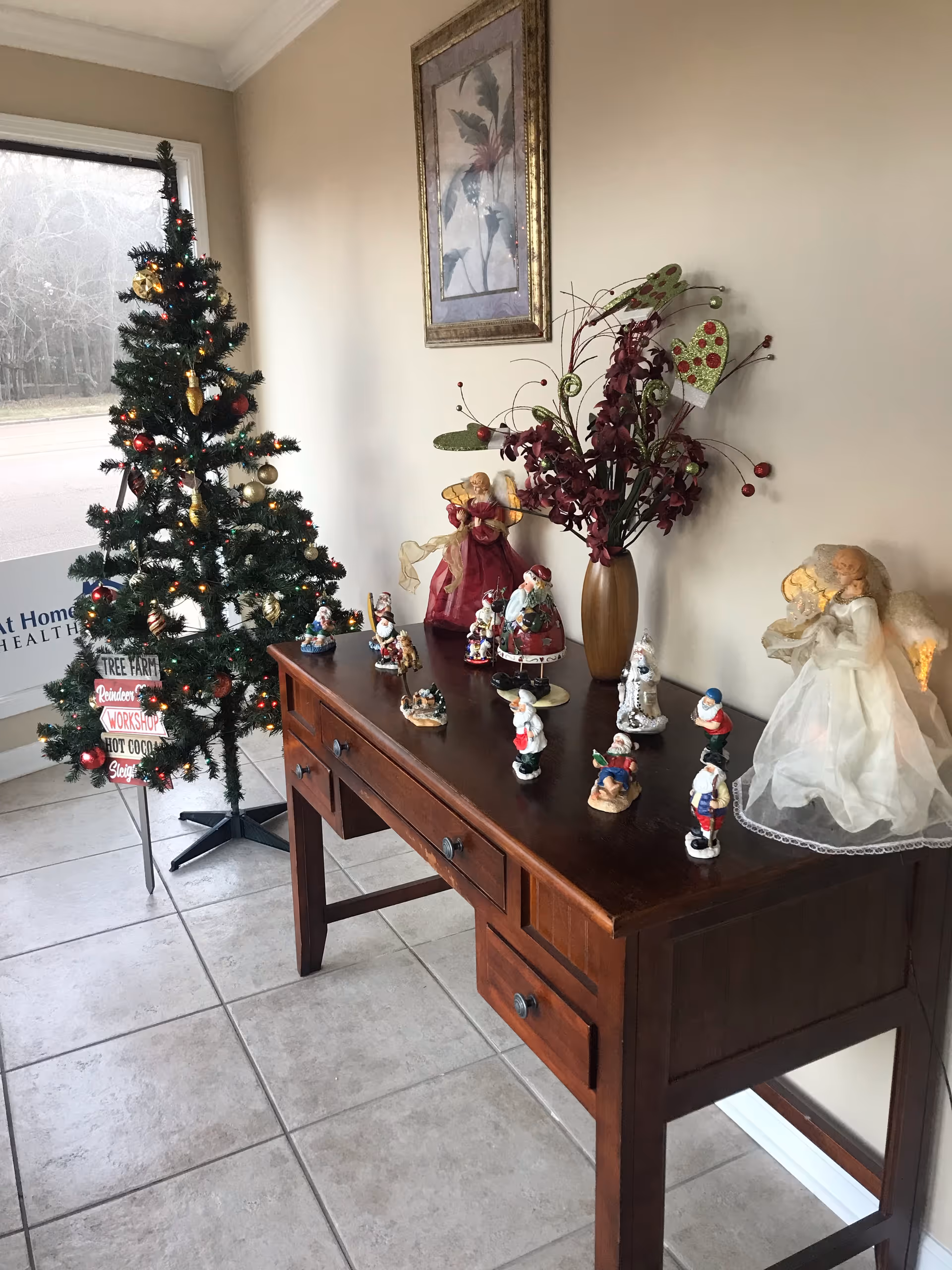 A Christmas tree and holiday decorations on a wooden console table in a bright hallway.