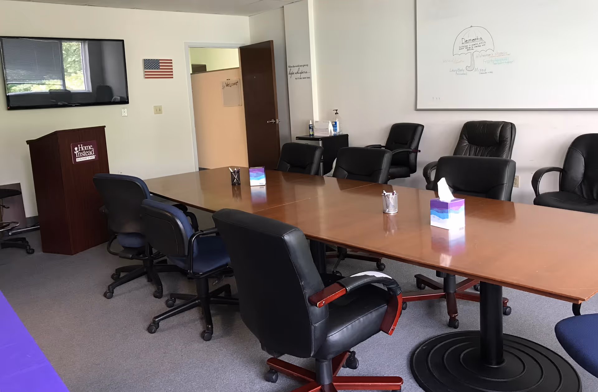 Large conference room with a long table, black chairs, podium, and wall-mounted screen.