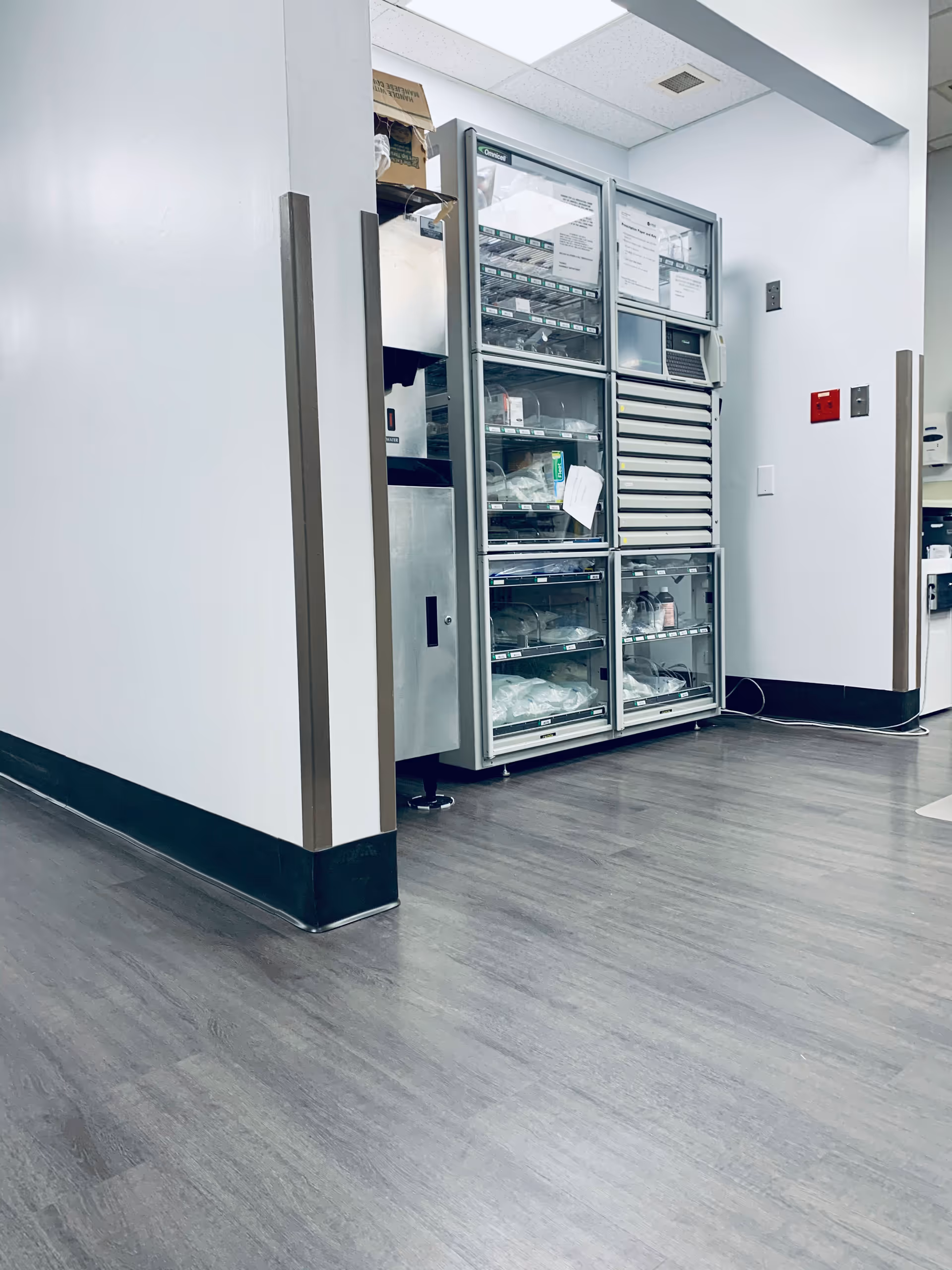 Glass-door medical refrigeration units line a clean hospital corridor with storage shelves.