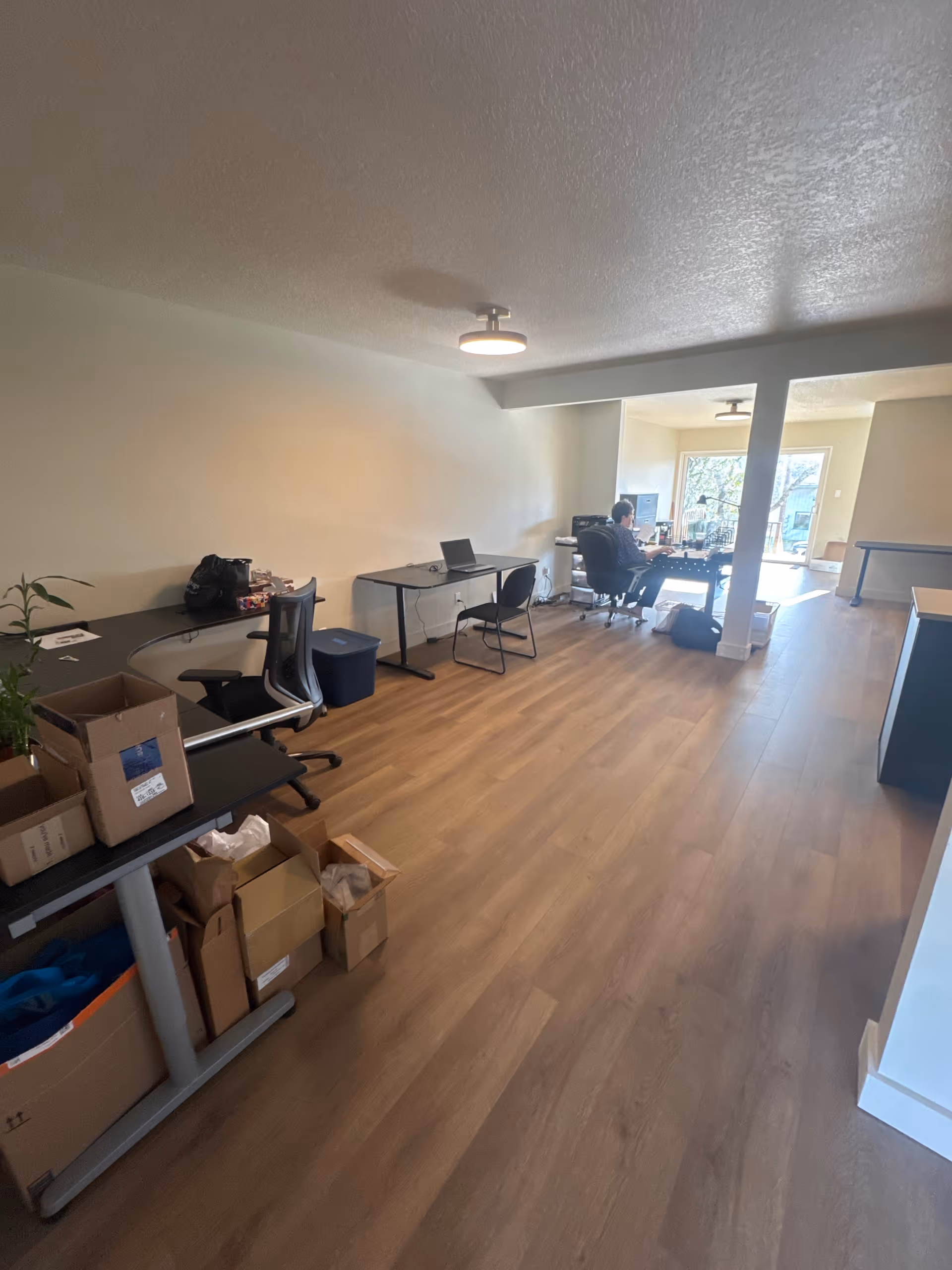 Interior office-like room with desks, chairs, and a person working at a laptop.