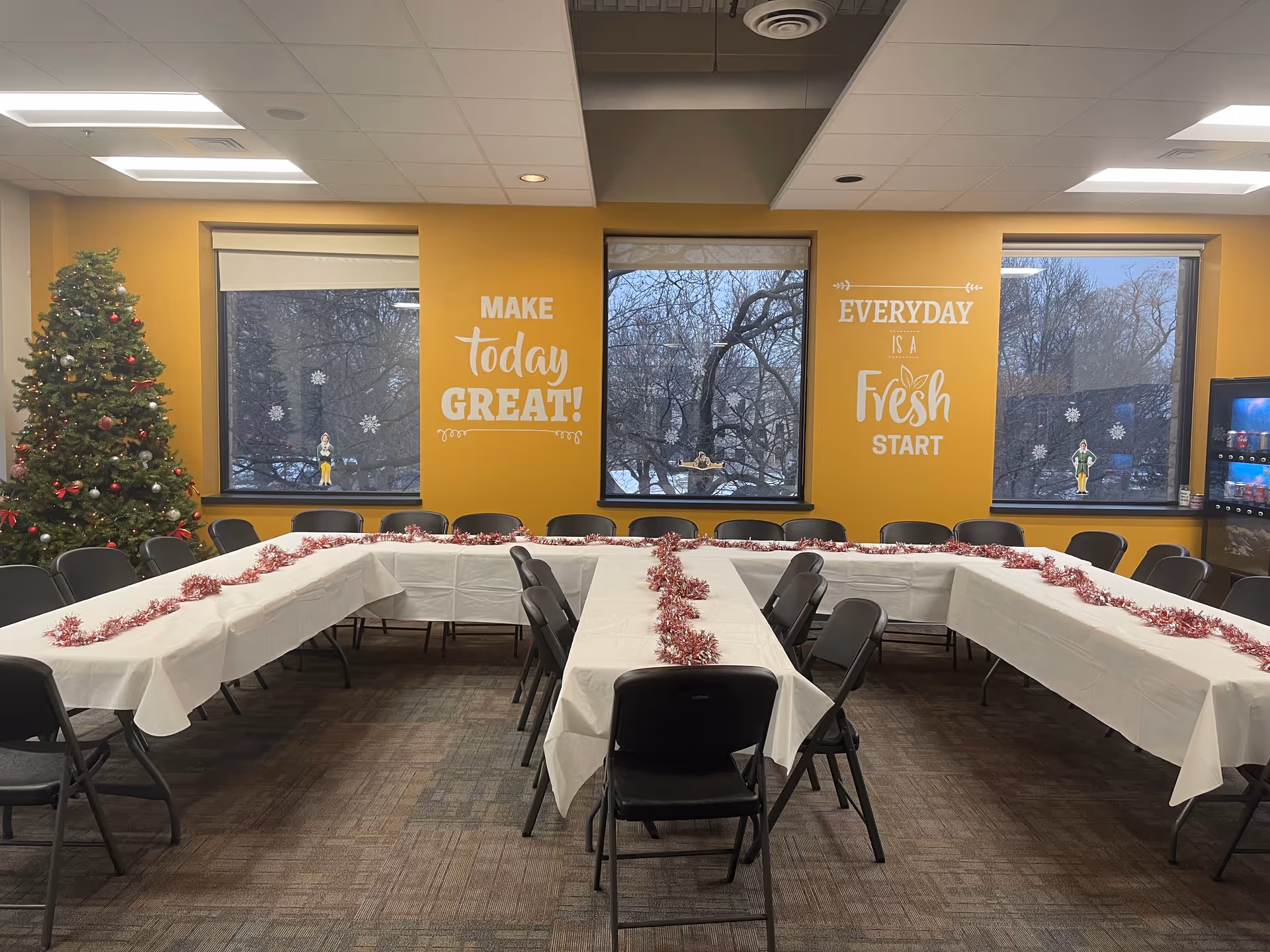Interior banquet dining hall with U-shaped tables, garland, Christmas tree, and yellow inspirational walls.