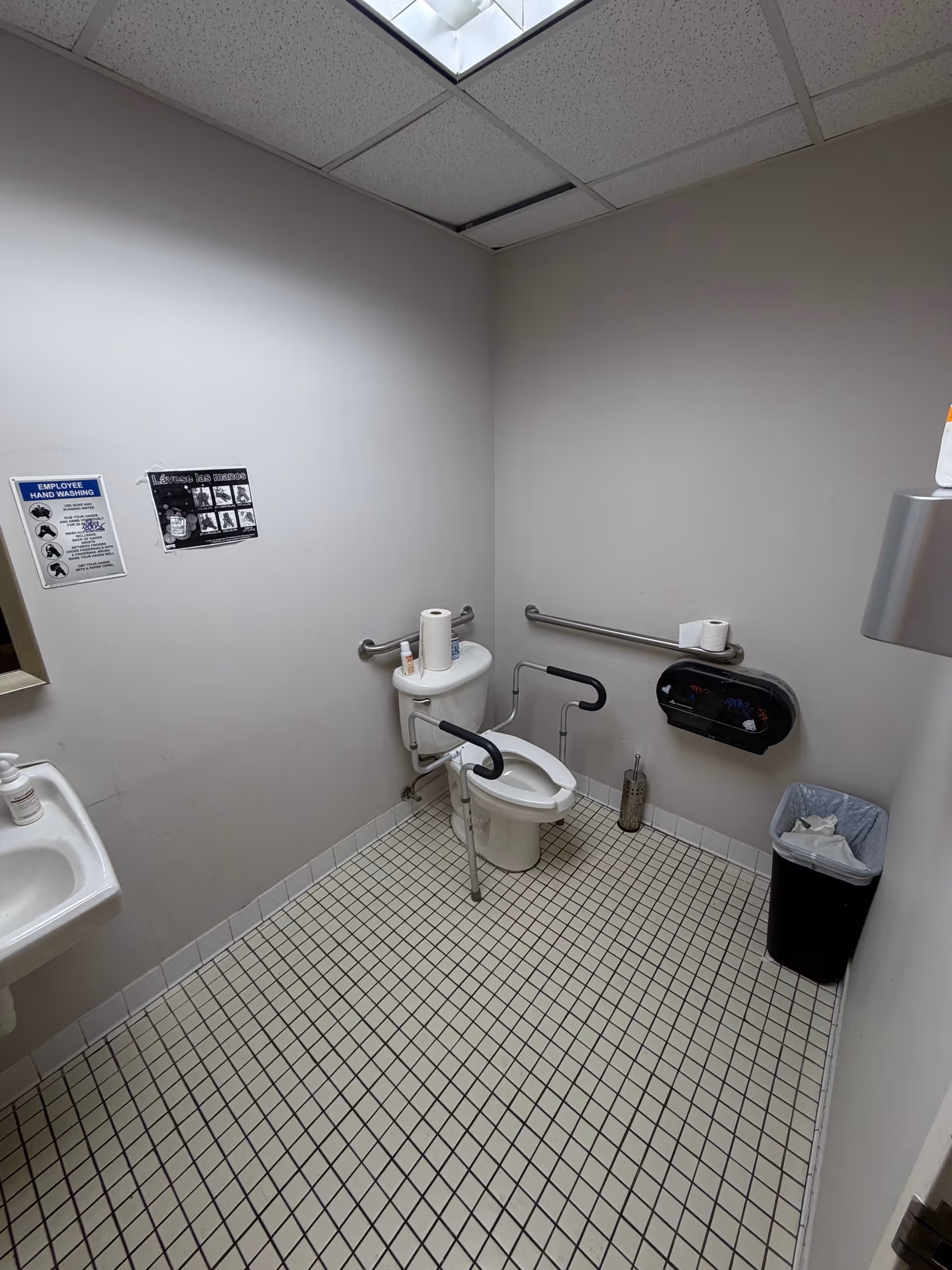 Accessible bathroom with toilet, grab bars, sink, and a trash bin.