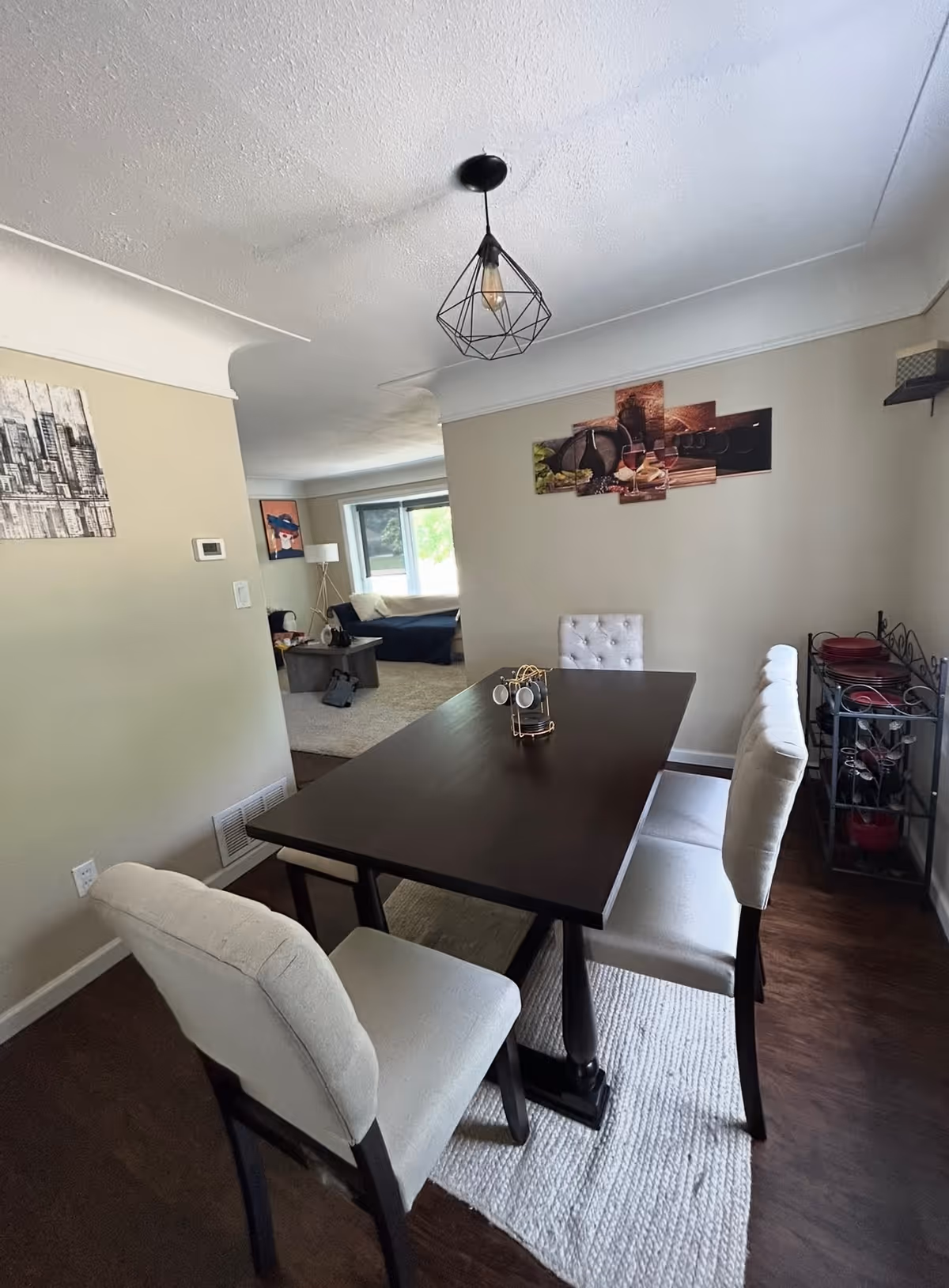 Dining room with a dark table, four white chairs, wall art, and a nearby living area.