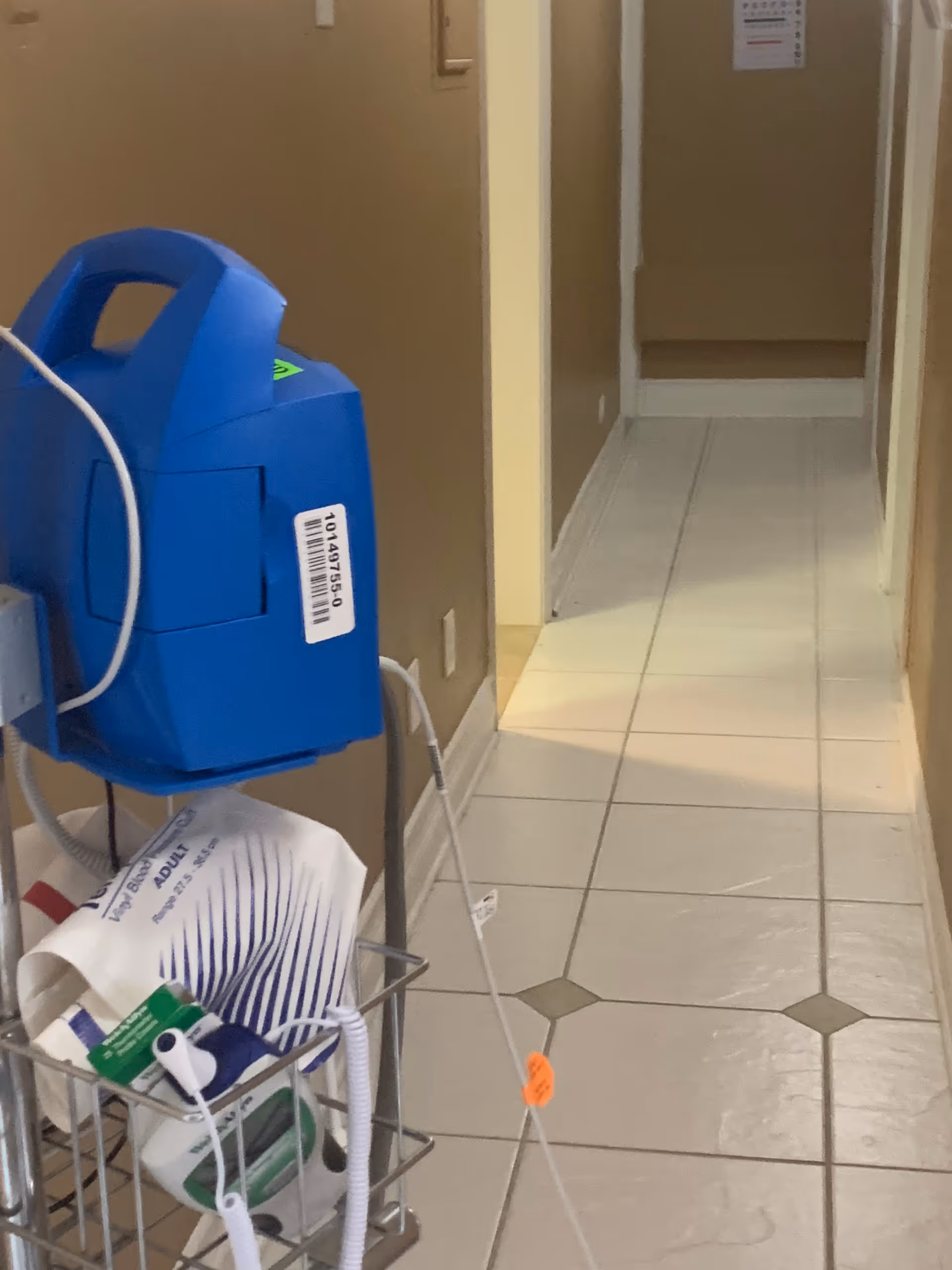 Narrow clinic hallway with a blue medical device and supply cart.