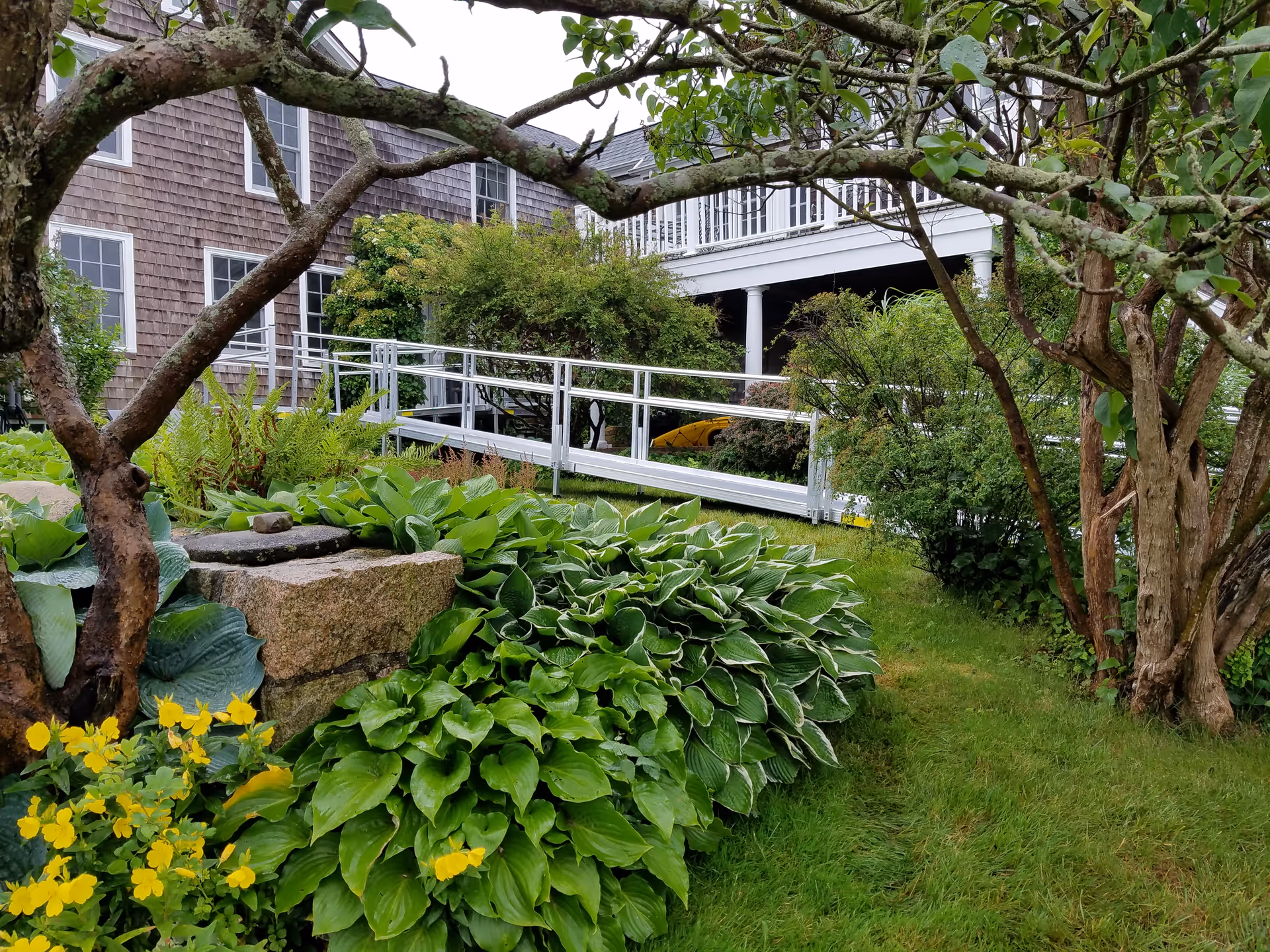 Exterior of a senior living facility with a white ramp and lush garden.