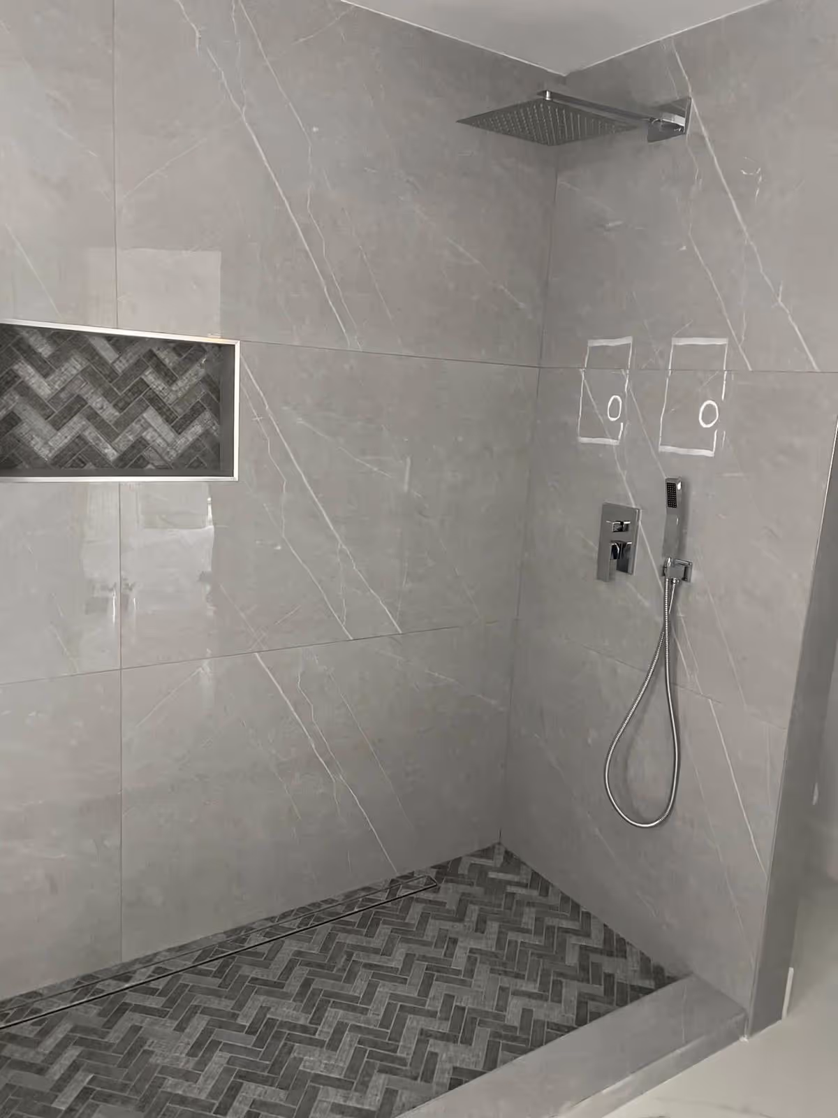 Modern gray-tiled bathroom with a rainfall shower, handheld sprayer, and a recessed niche.