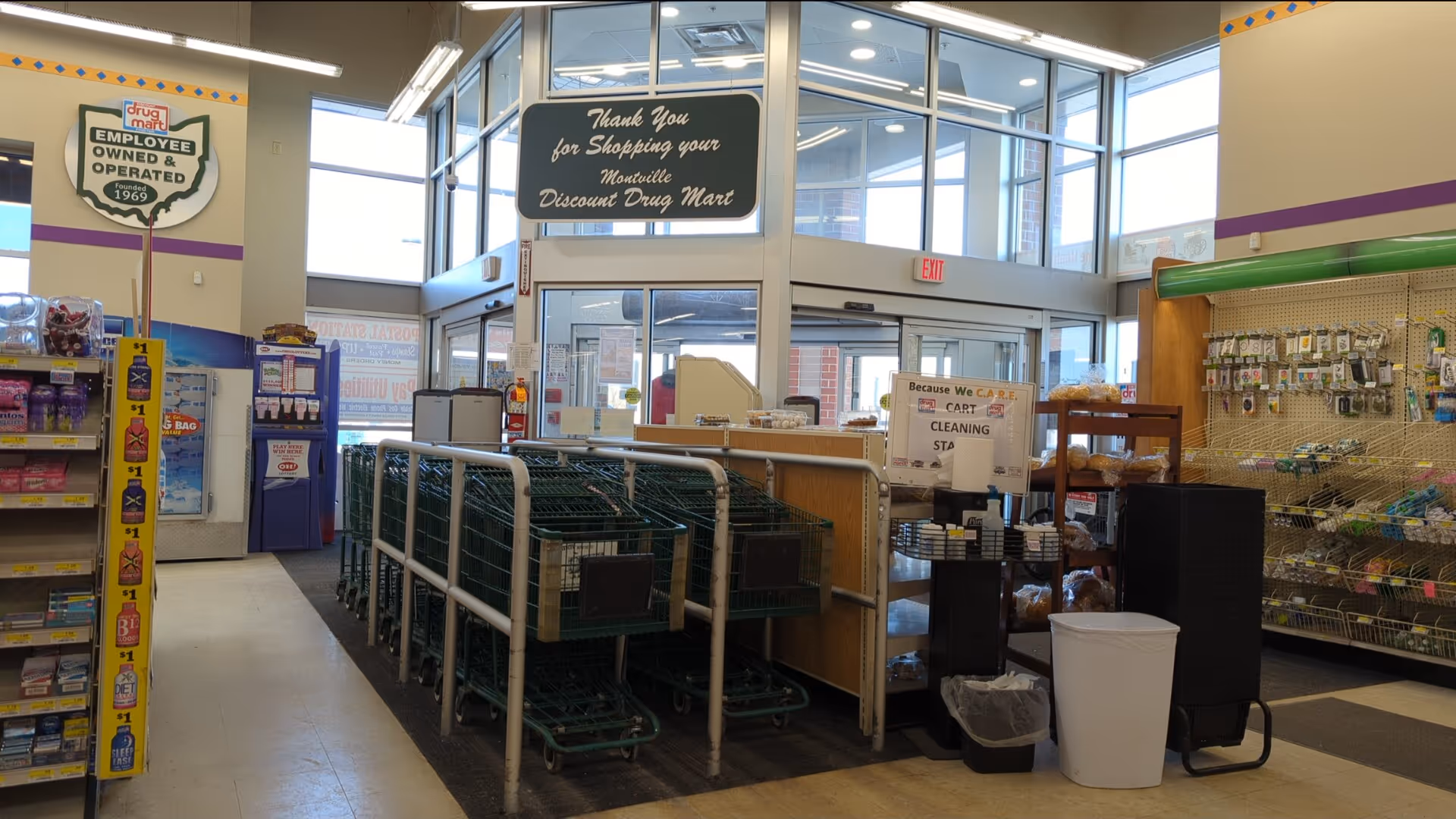 Inside a Discount Drug Mart, shopping carts line a central aisle near checkout.