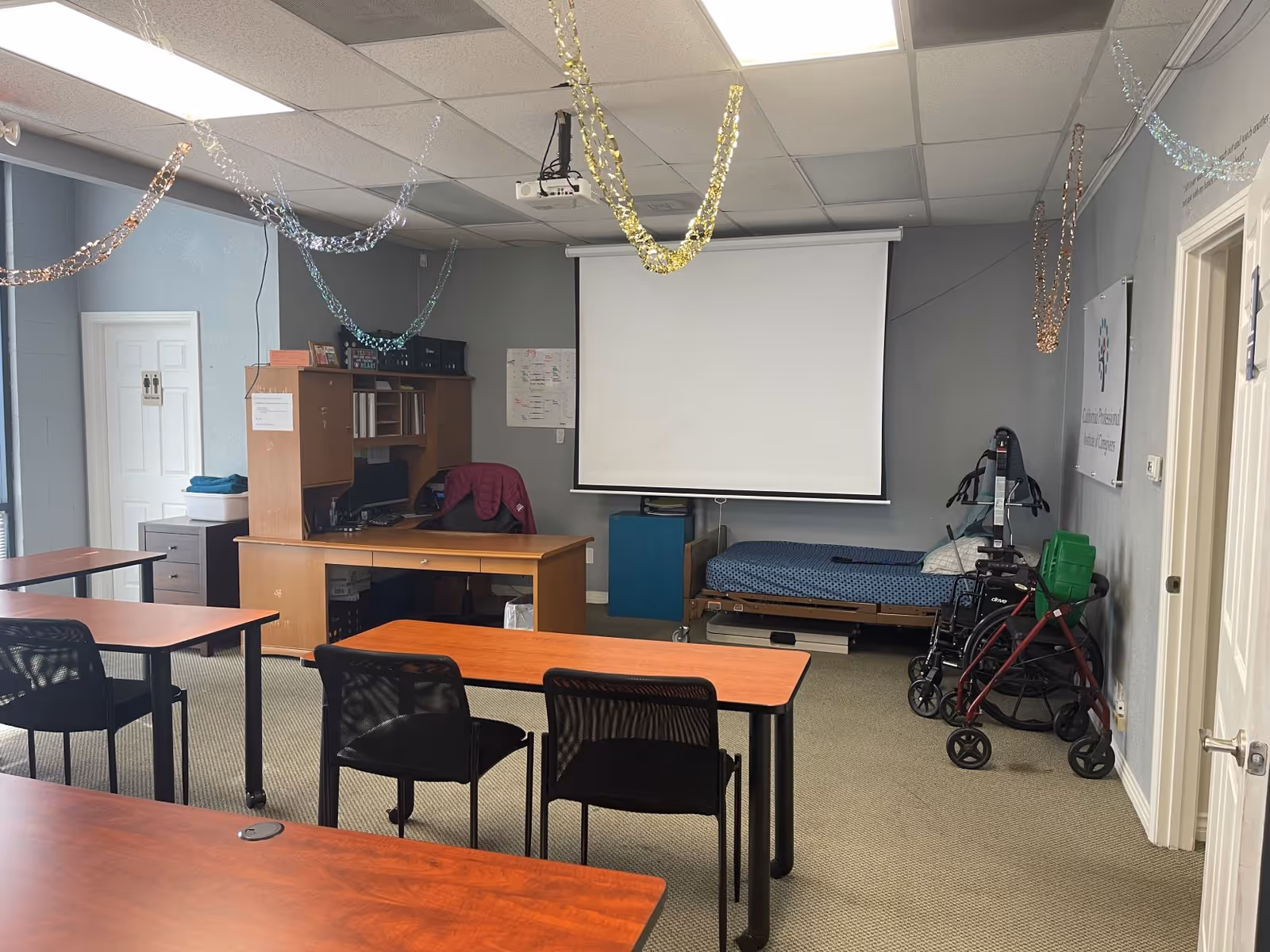 Classroom-style activity room with desks, projector screen, and medical equipment in a senior care facility.