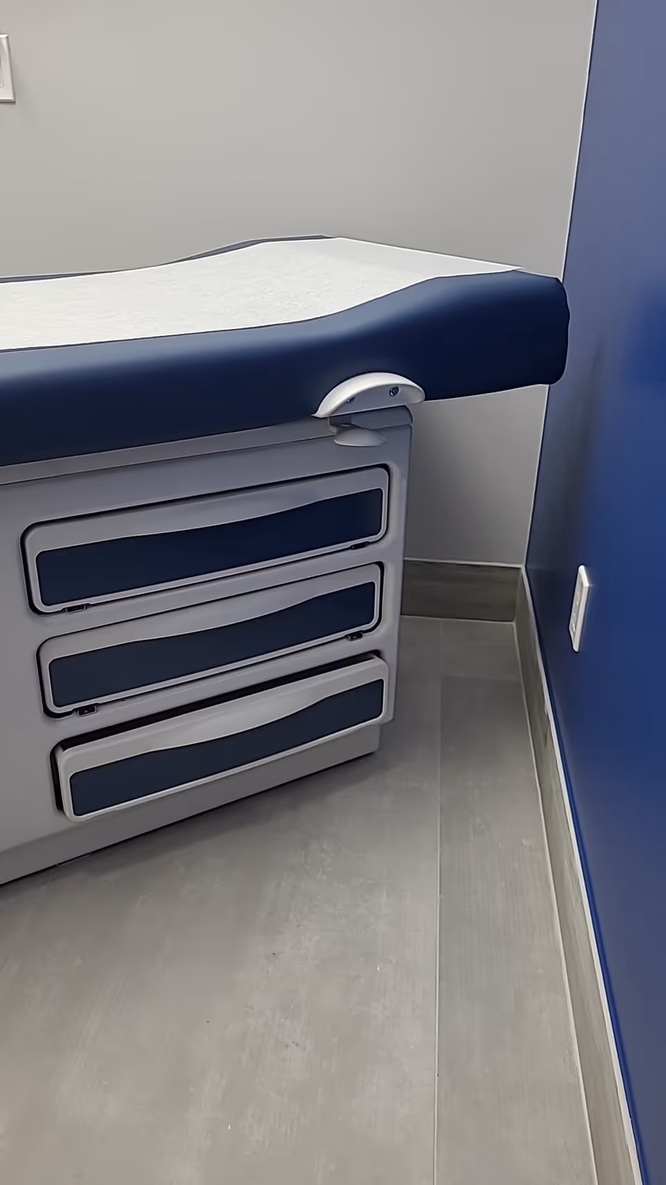 Blue padded examination table with drawers in a small clinical room.