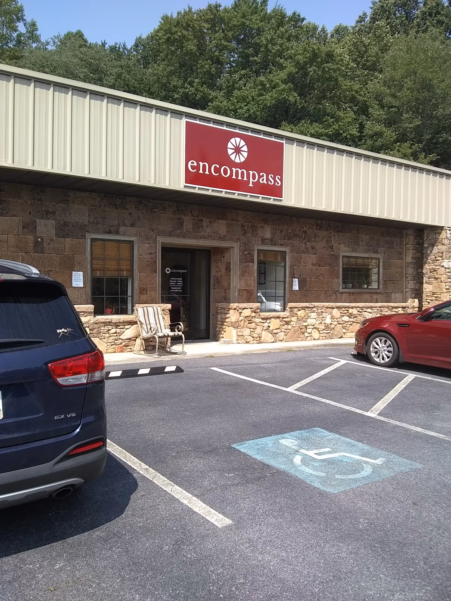 Exterior view of a stone-front building entrance with a red Encompass sign and parked cars.