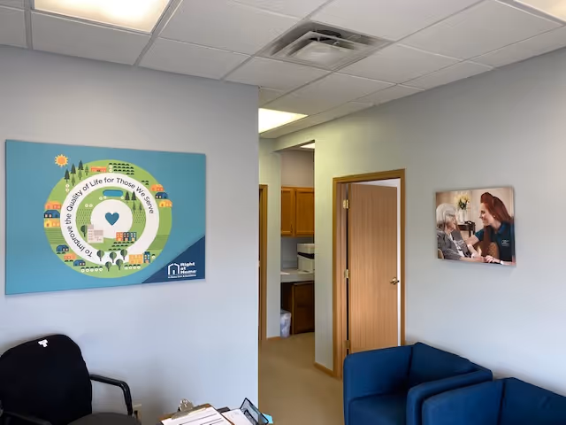 Light blue lobby area with blue chairs, wall poster, and doorway to kitchenette.