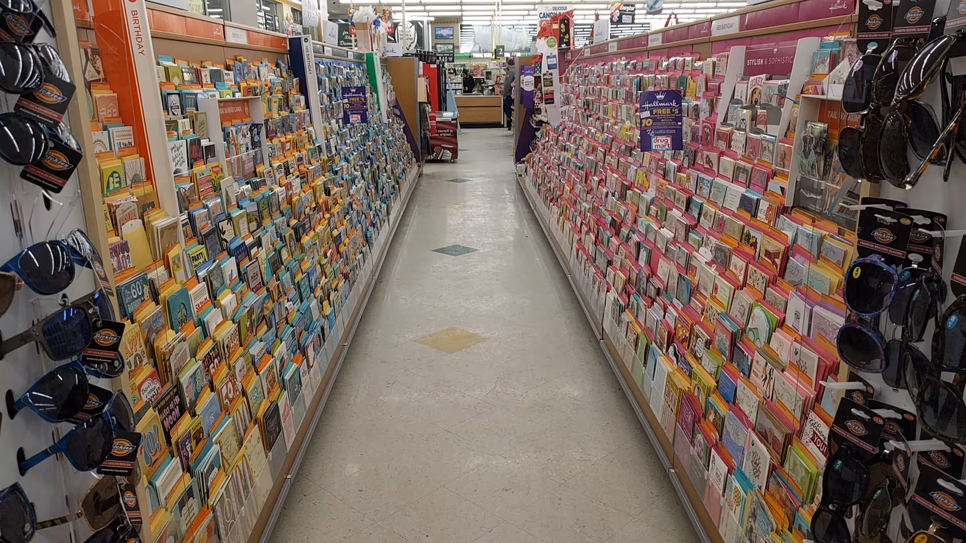 Inside Discount Drug Mart, an aisle displays colorful greeting cards along both sides.