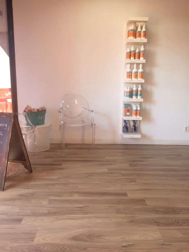 Clear acrylic chair beside a shelf of lice treatment bottles in a bright interior.