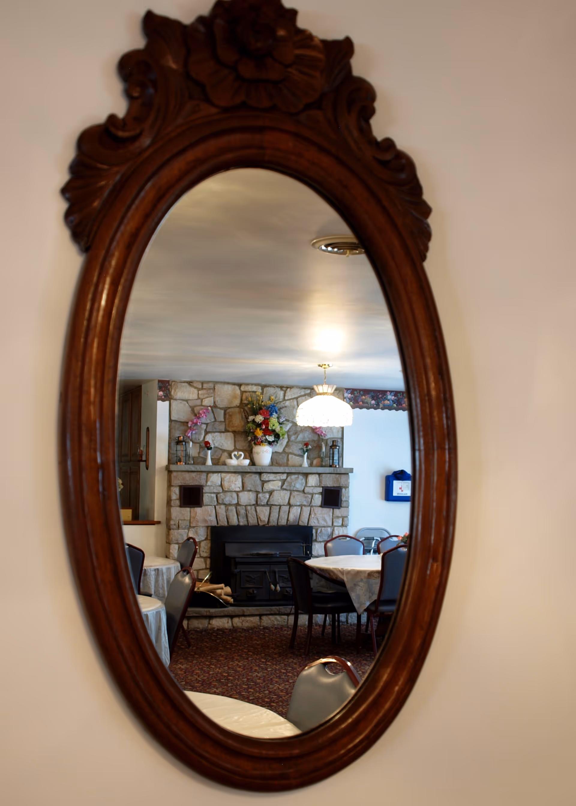 Ornate wooden mirror reflects a stone fireplace and dining room.