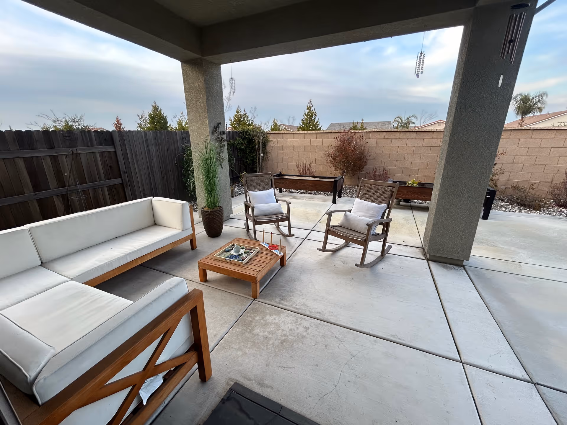 Covered outdoor patio with white cushioned seating, two rocking chairs, and a coffee table.