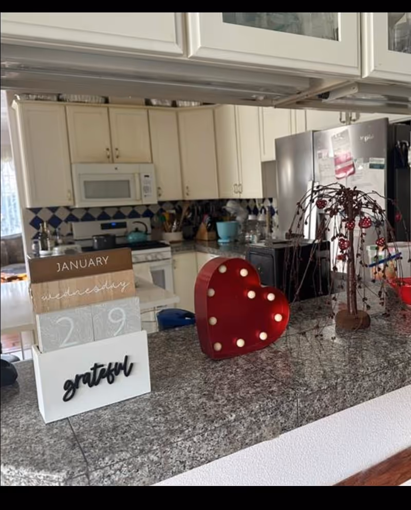 Bright kitchen with white cabinets, stainless steel fridge, and festive heart decoration on granite counter.