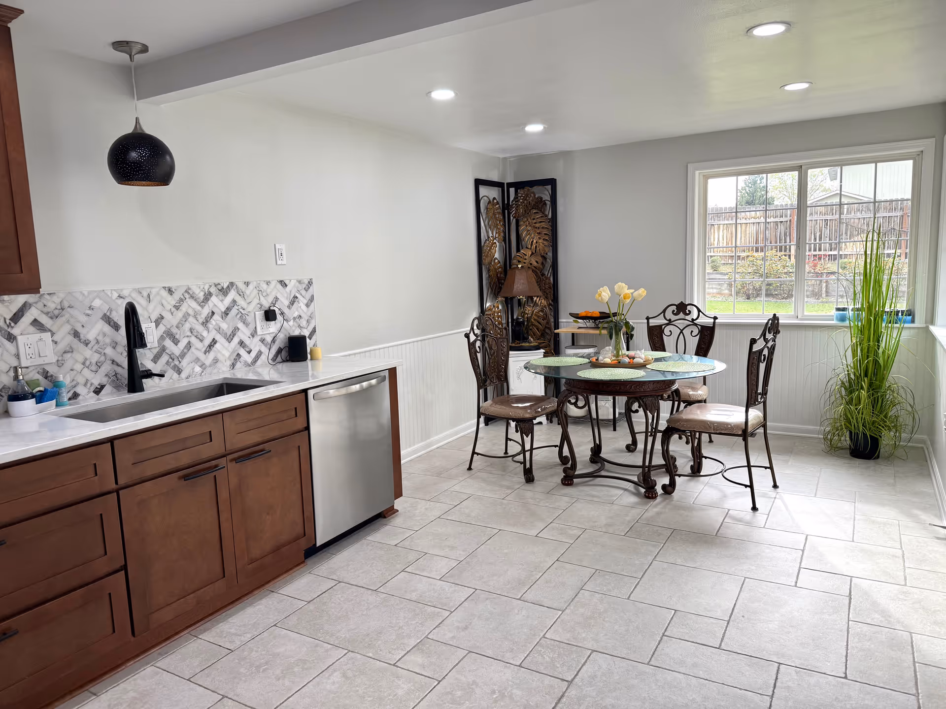 Open kitchen and dining area with dark wood cabinets, glass table, and plants.
