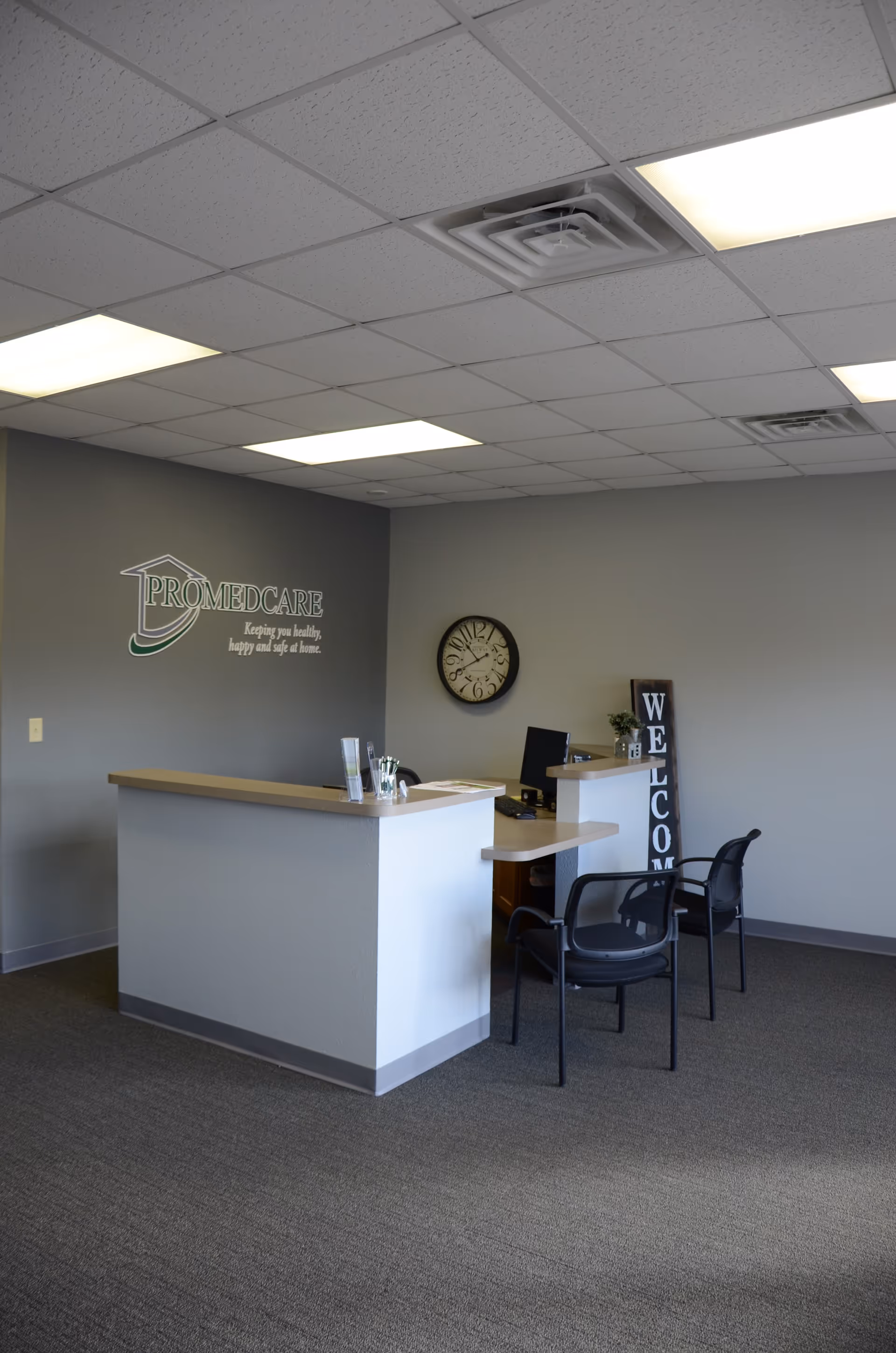 Interior reception area with PROMEDCARE logo, desk, chairs, and welcome sign.