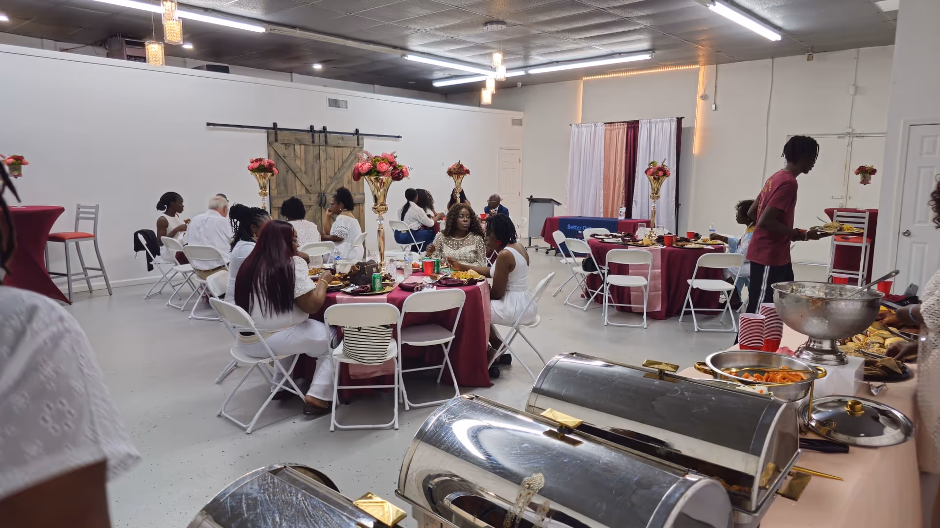 A dining hall filled with residents and staff around round tables with pink tablecloths.