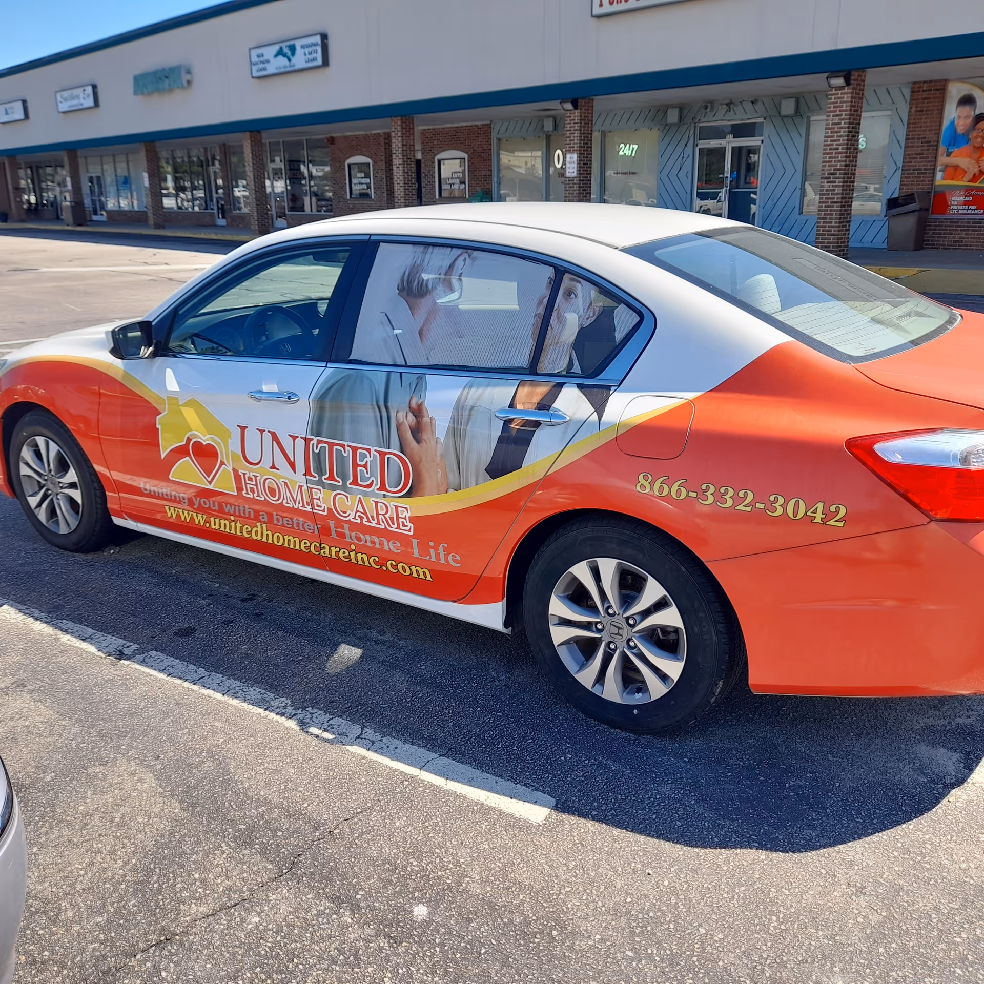 A branded United Home Care car parked in a strip mall parking lot.