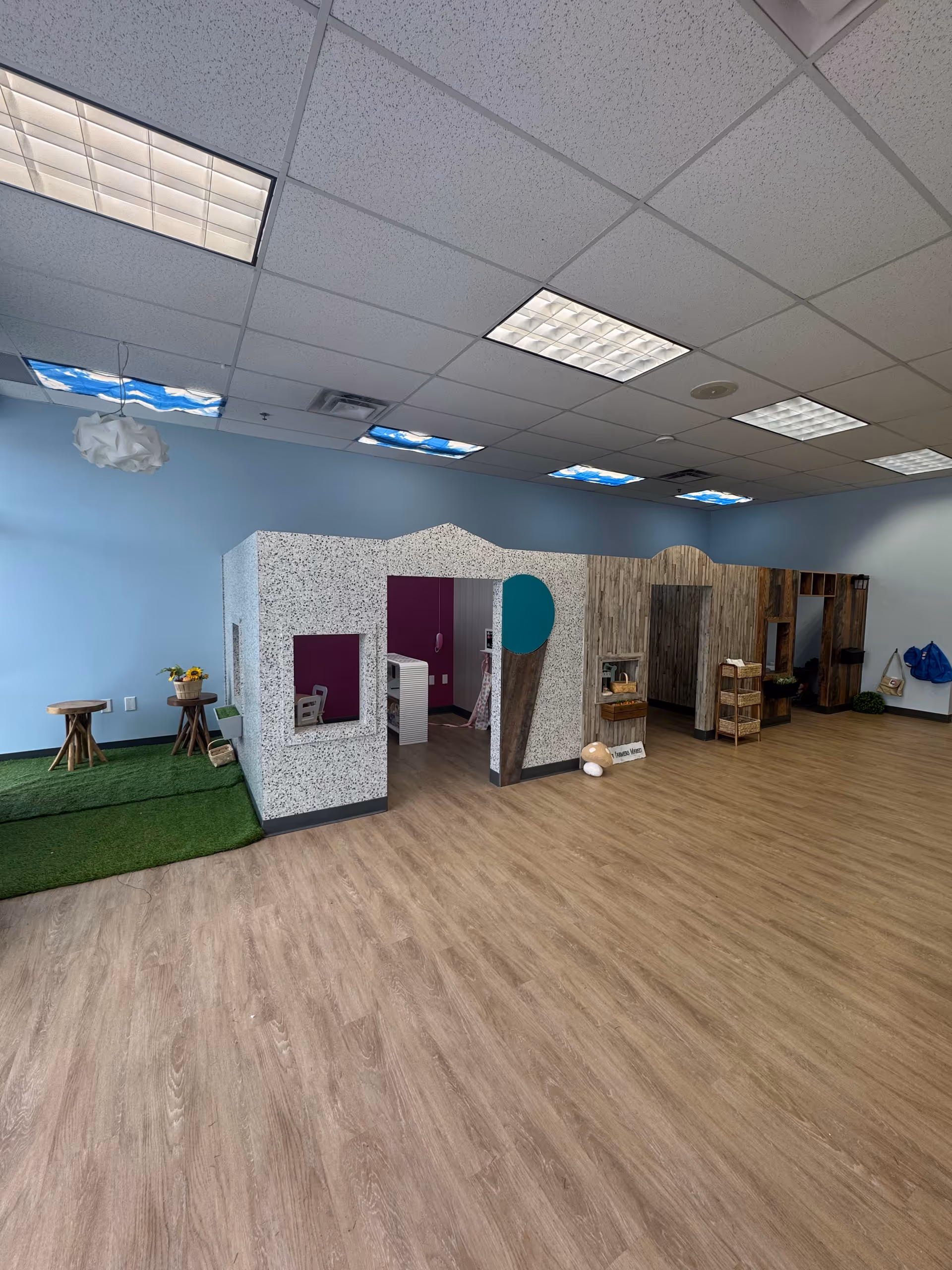 Interior ABA therapy play space with partitioned cubicles, grass mat, and wooden flooring.