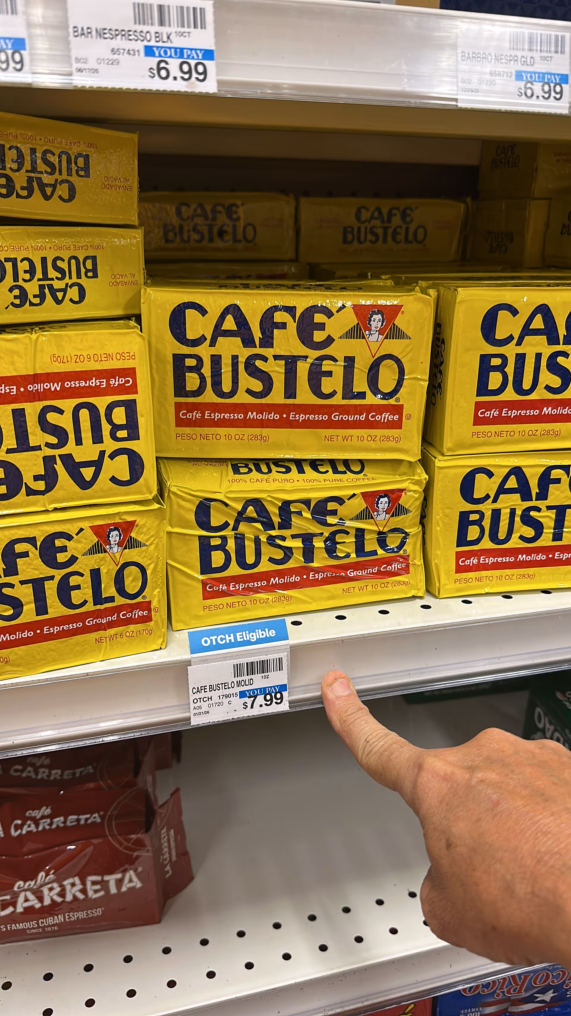 Close-up of Café Bustelo coffee boxes on a store shelf, with a hand pointing.