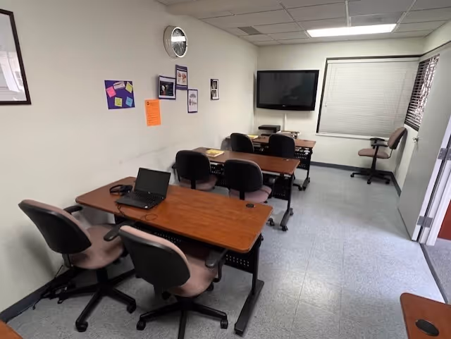 Training room in BAYADA Assistive Care with wooden tables, chairs, a laptop, and a wall screen.