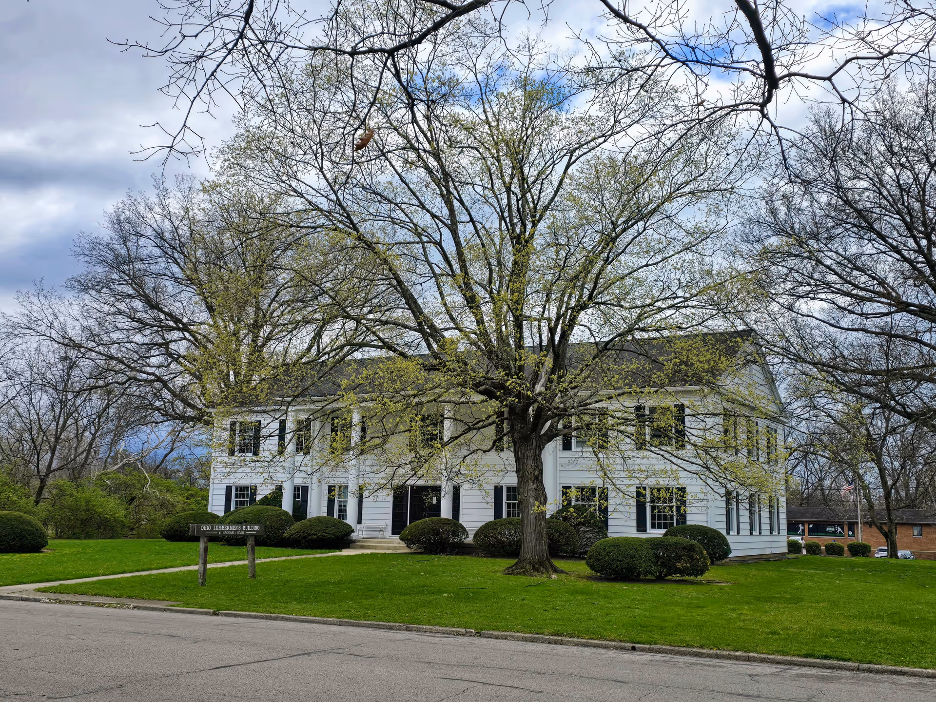 White two-story building with a large tree, trimmed bushes, and a green lawn.