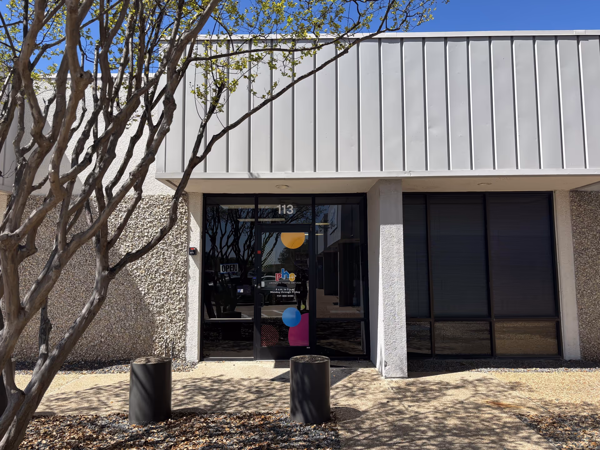 Front entrance of beige building with glass doors, large windows, and colorful shapes on door.