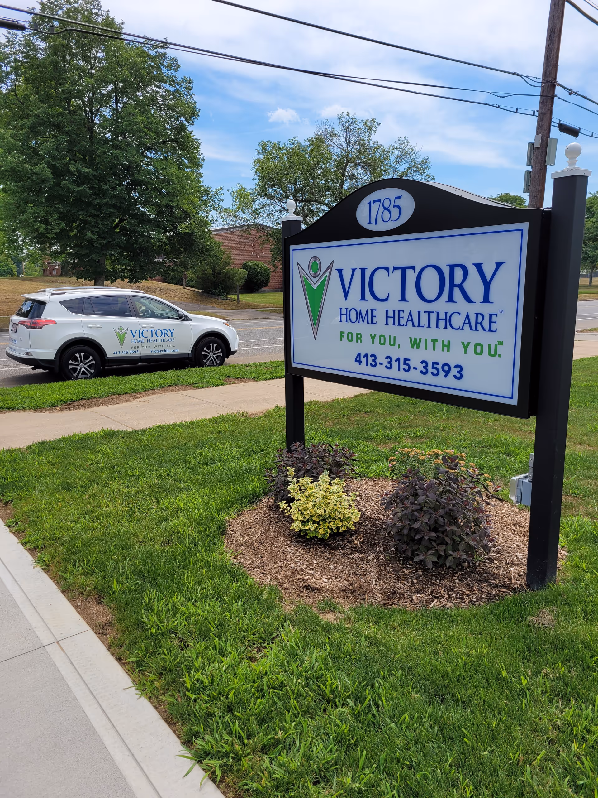 Outdoor scene with Victory Home Healthcare sign, landscaped bed, and a white service vehicle.