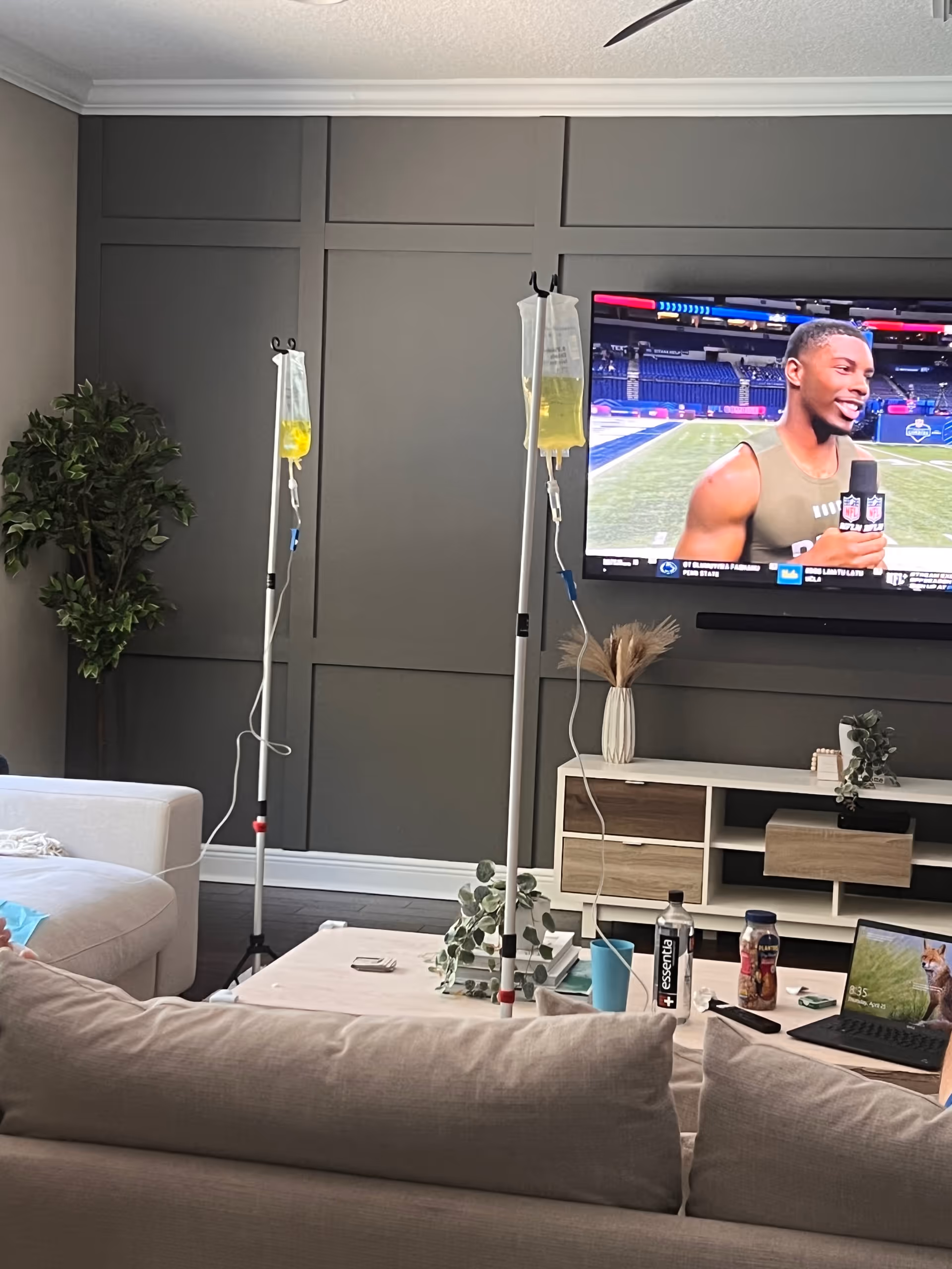 Living room with two IV drip stands beside a couch and a wall-mounted TV.