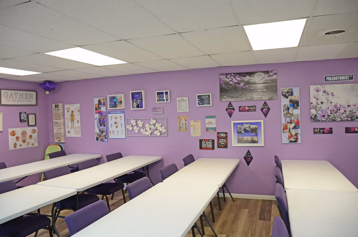 Purple-walled activity room with long white tables and purple chairs.